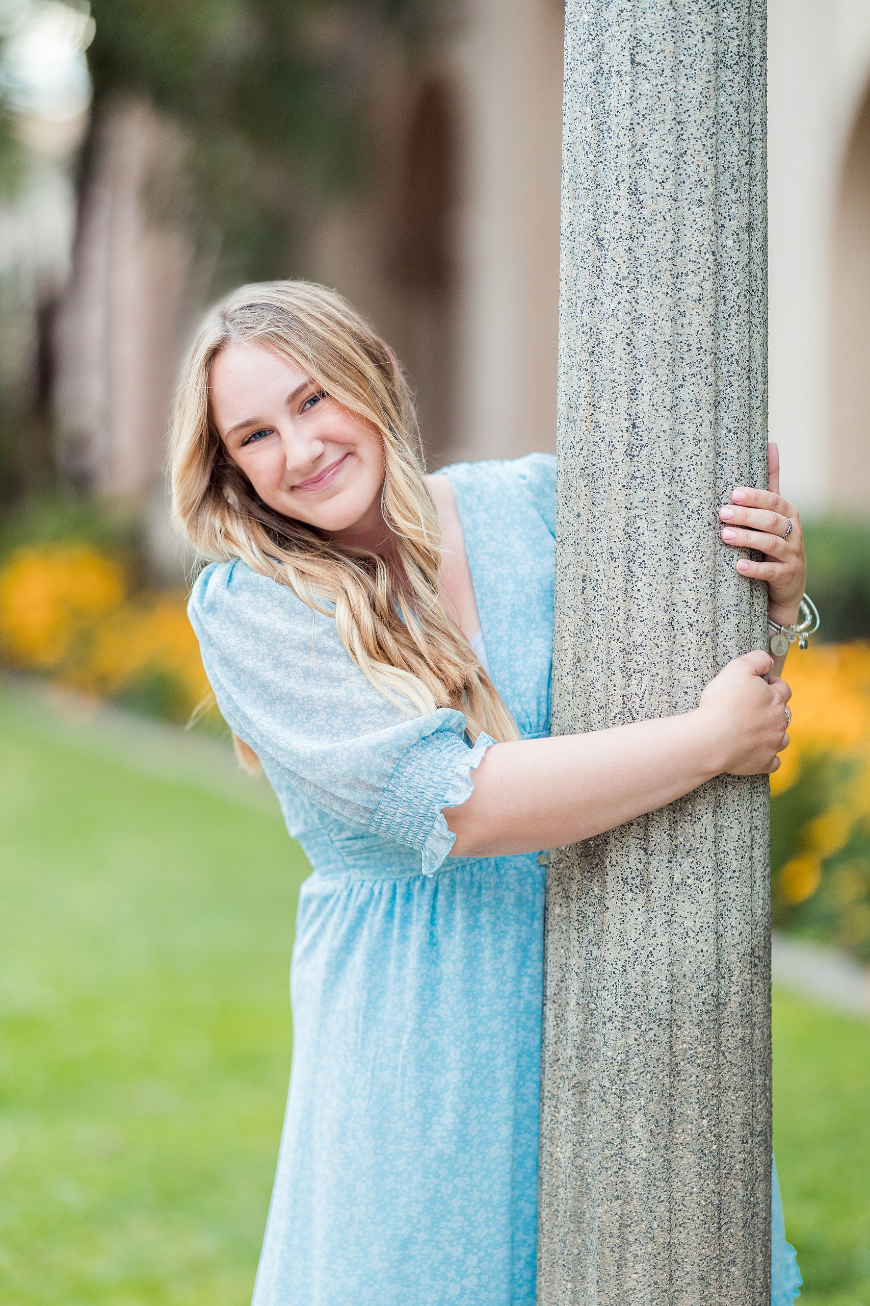 Balboa Park Senior Photography Session — 16 Senior in blue dress on bench with white flowering plant in immediate foreground