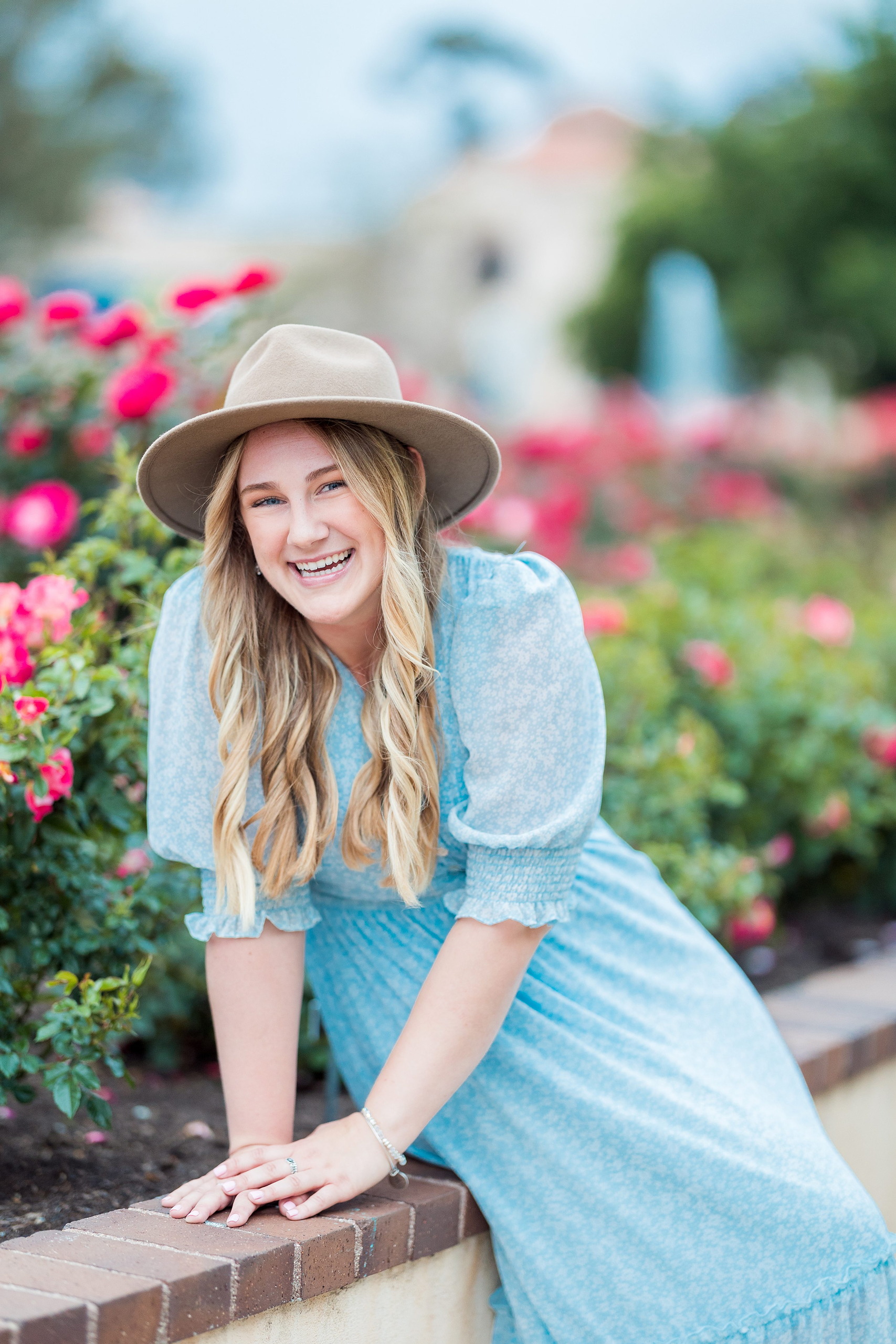 Balboa Park Senior Photography Session — 18 Senior in blue dress on grass wearing white cardigan and tan hat, pink flowers behind