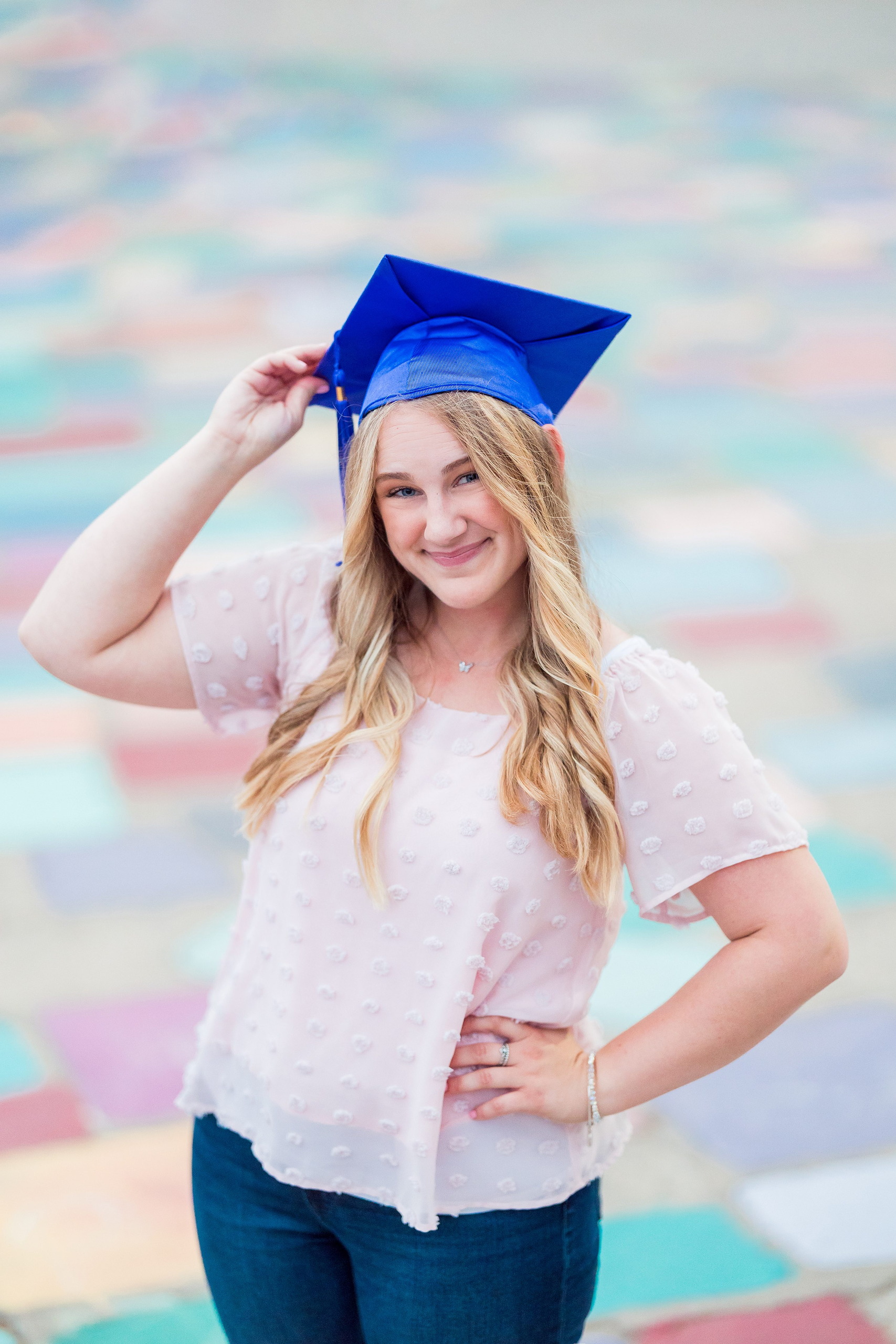Balboa Park Senior Photography Session — 21 Senior wearing blue graduation cap in pink top standing before colorful paint mural
