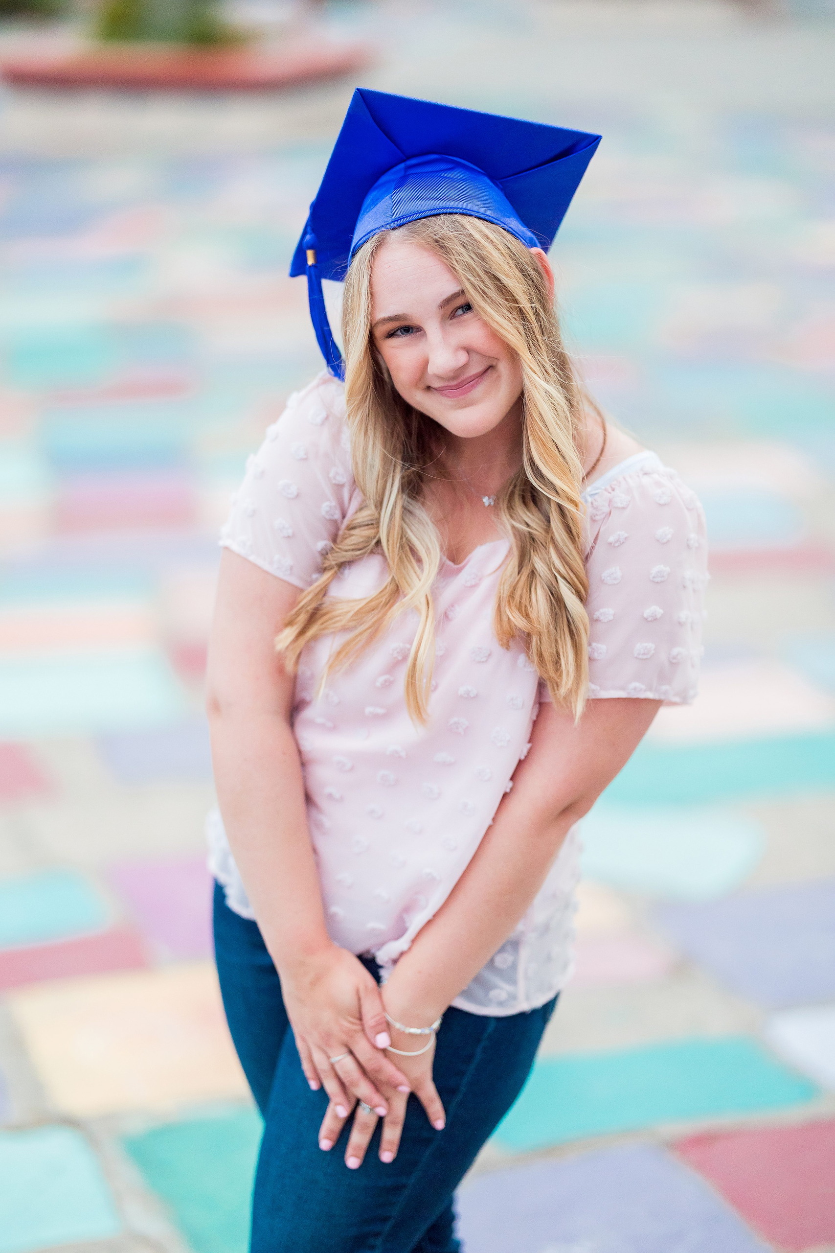 Balboa Park Senior Photography Session — 22 Senior with blue graduation cap tilted to side, pink top, colorful painted background
