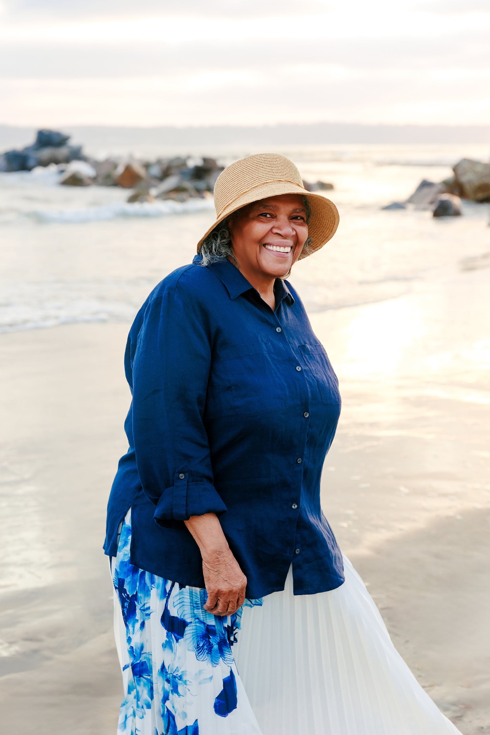 Because Time Flies: Family Photos on Coronado — 15 Bettie wears a straw hat and blue shirt on Coronado beach near rocks