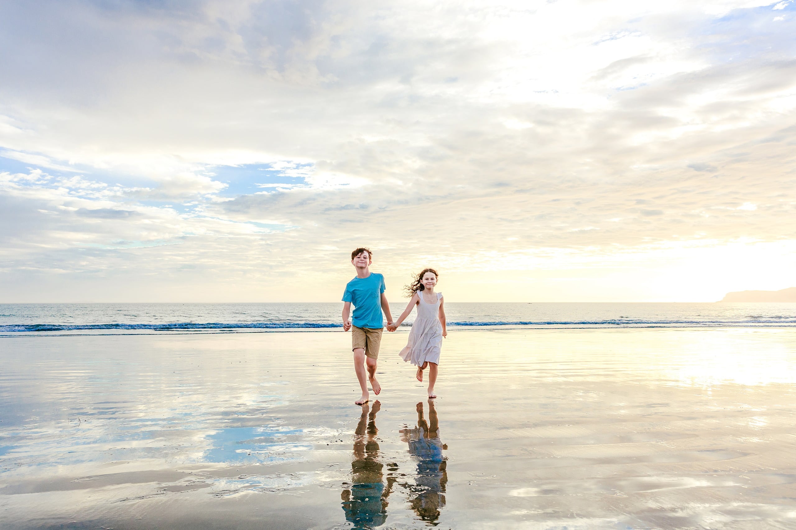 Behind the Scenes of Grammy Judy’s 80th Birthday Session: An Interview with Wendy — 03 Two children run hand in hand through shallow water as sun glows on the horizon