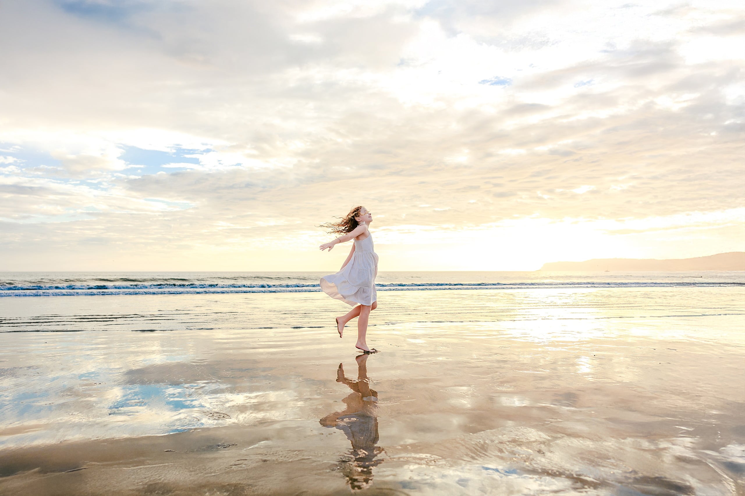 Behind the Scenes of Grammy Judy’s 80th Birthday Session: An Interview with Wendy — 04 Woman in white dress runs across beach with hair flying, backlit by golden sunset