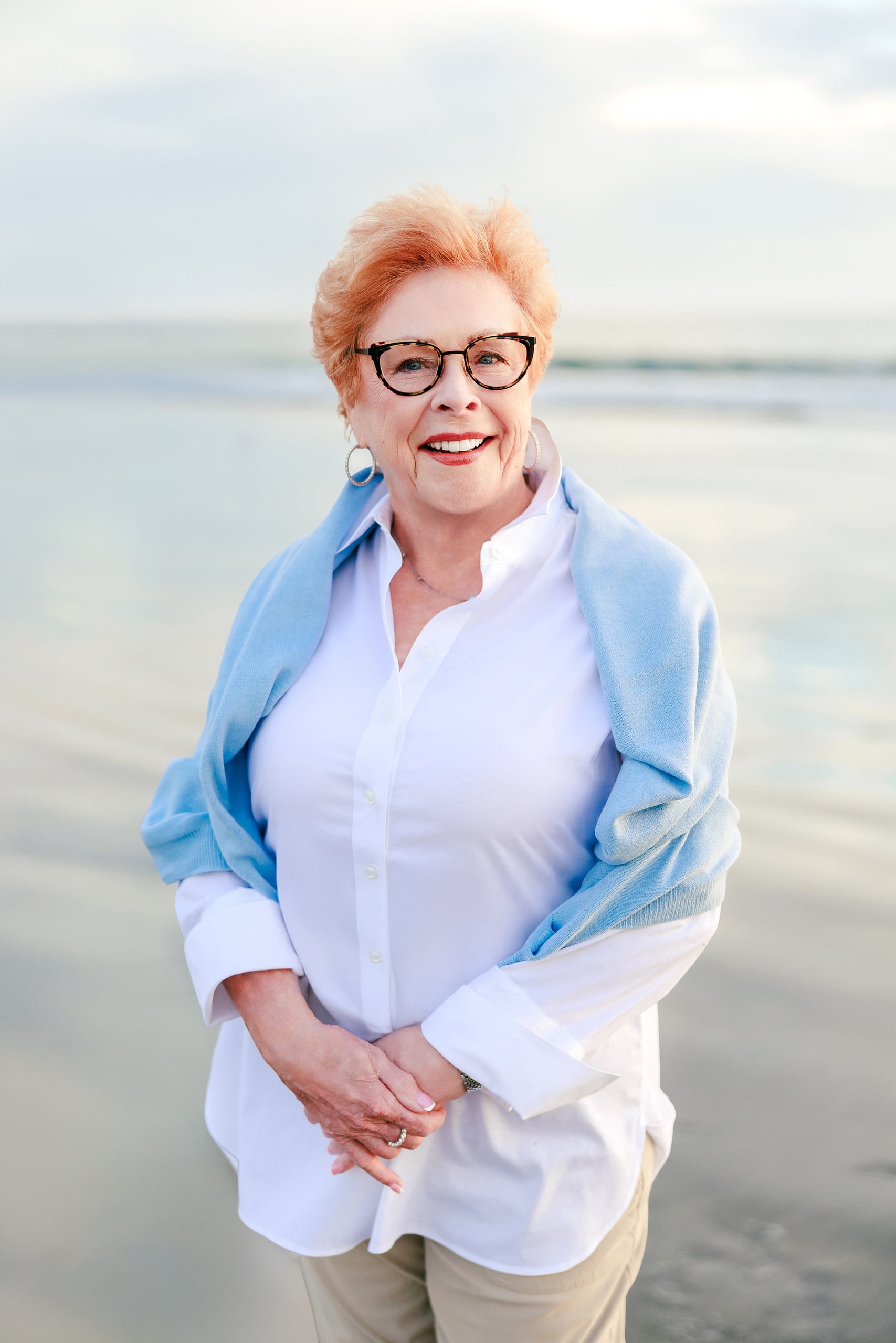 Behind the Scenes of Grammy Judy’s 80th Birthday Session: An Interview with Wendy — 06 Close-up of Grammy Judy in blue cardigan on beach with calm ocean behind her