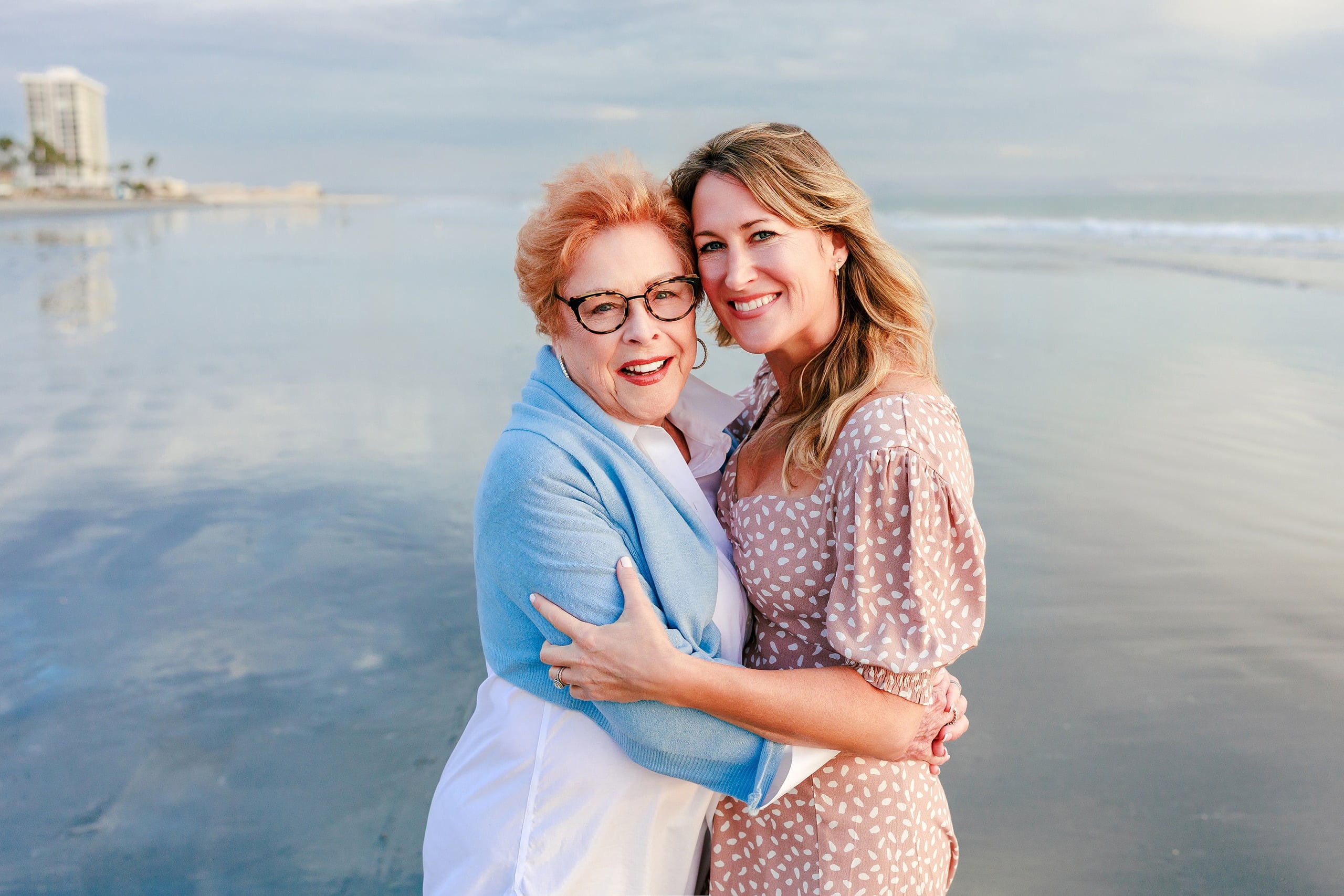 Behind the Scenes of Grammy Judy’s 80th Birthday Session: An Interview with Wendy — 08 Grammy Judy and woman embrace on beach with ocean and Hotel del Coronado visible
