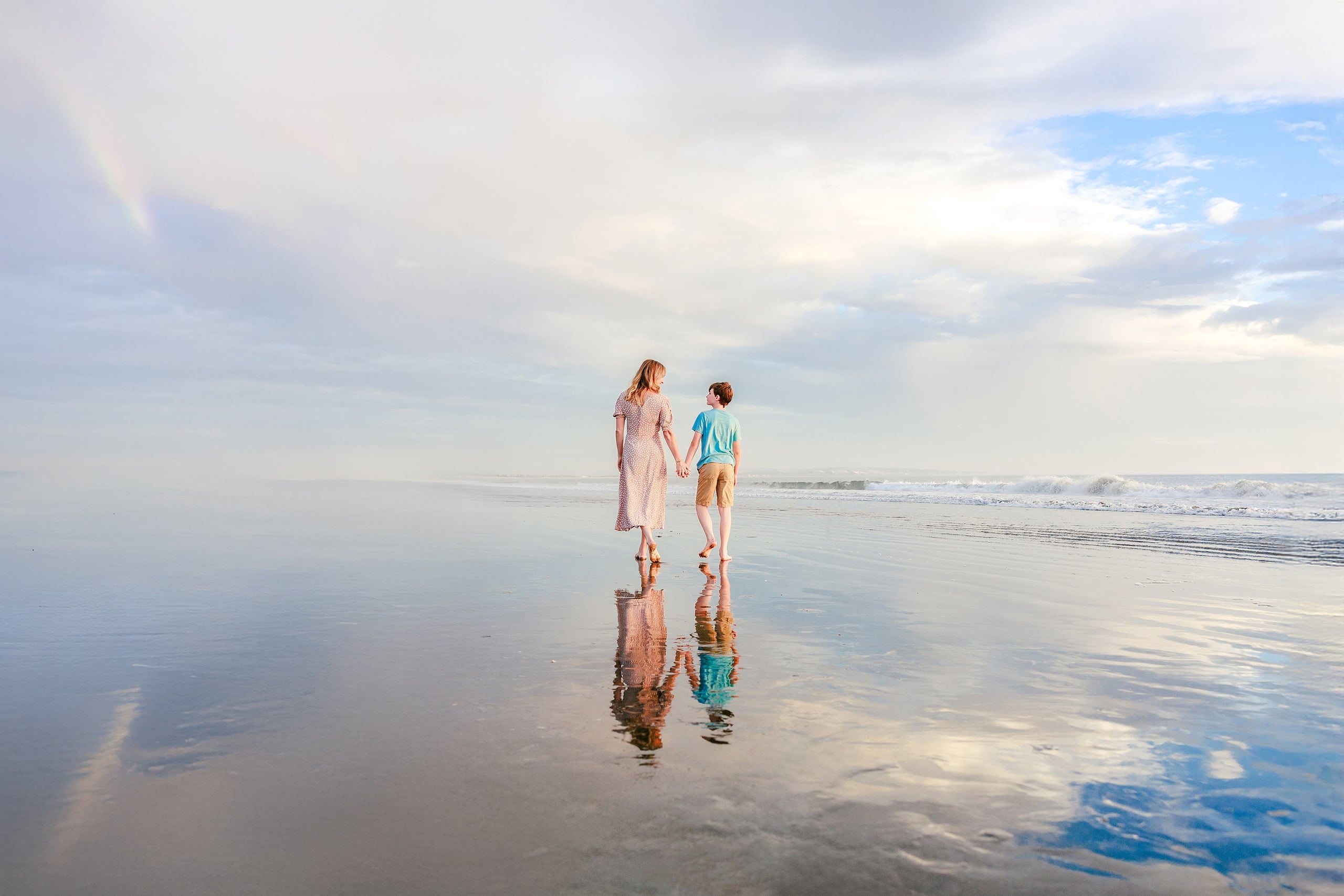 Behind the Scenes of Grammy Judy’s 80th Birthday Session: An Interview with Wendy — 12 Woman and boy stand on wet sand facing ocean, silhouetted against glowing golden light