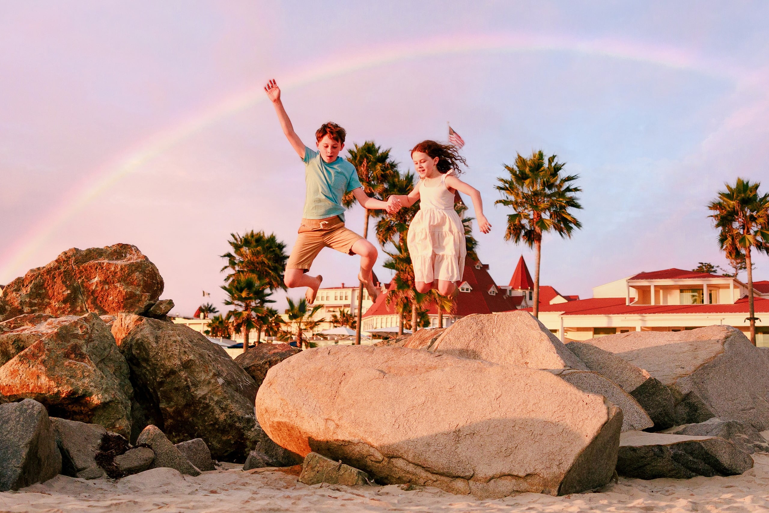 Behind the Scenes of Grammy Judy’s 80th Birthday Session: An Interview with Wendy — 18 Two children jump playfully on rocks with rainbow glowing in pink sky above