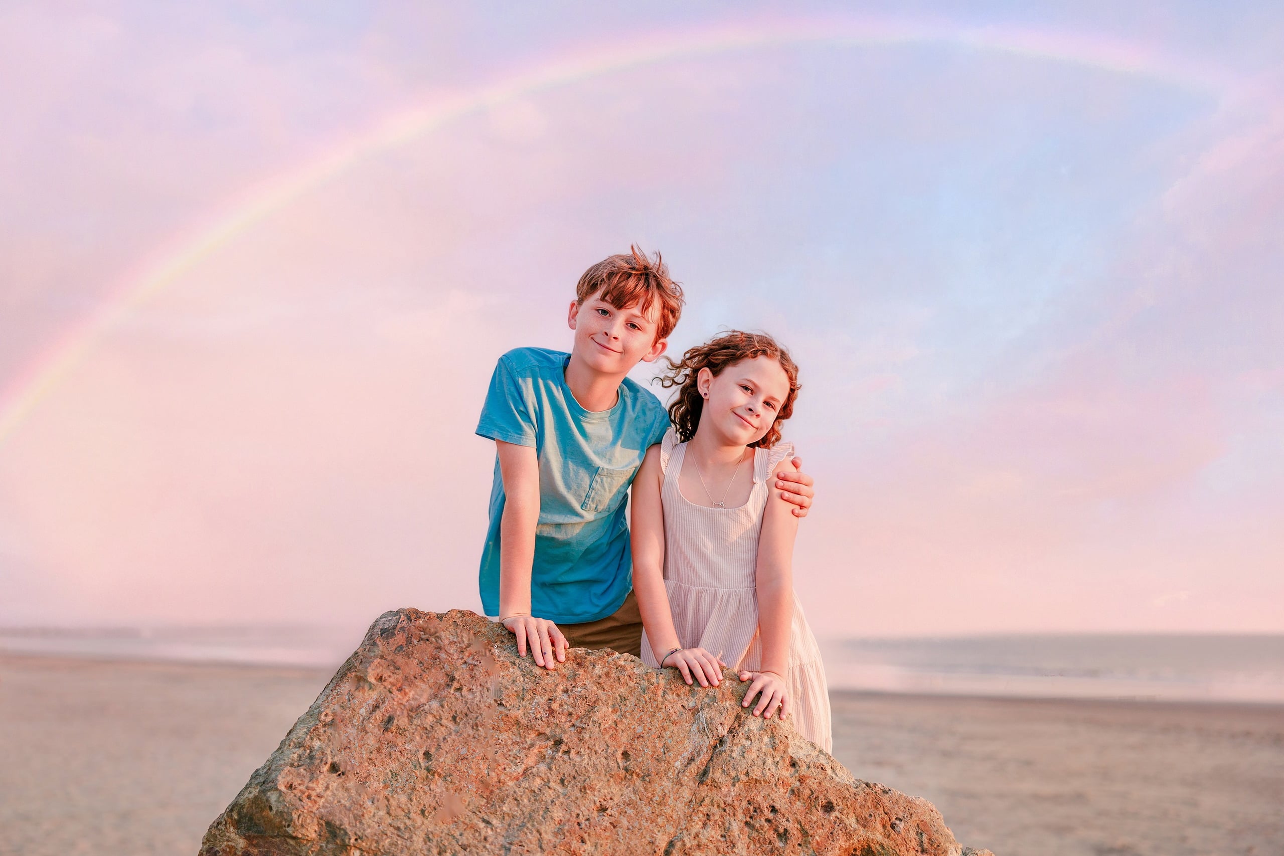 Behind the Scenes of Grammy Judy’s 80th Birthday Session: An Interview with Wendy — 21 Boy and girl sit together on rock with rainbow arcing through soft pink sky
