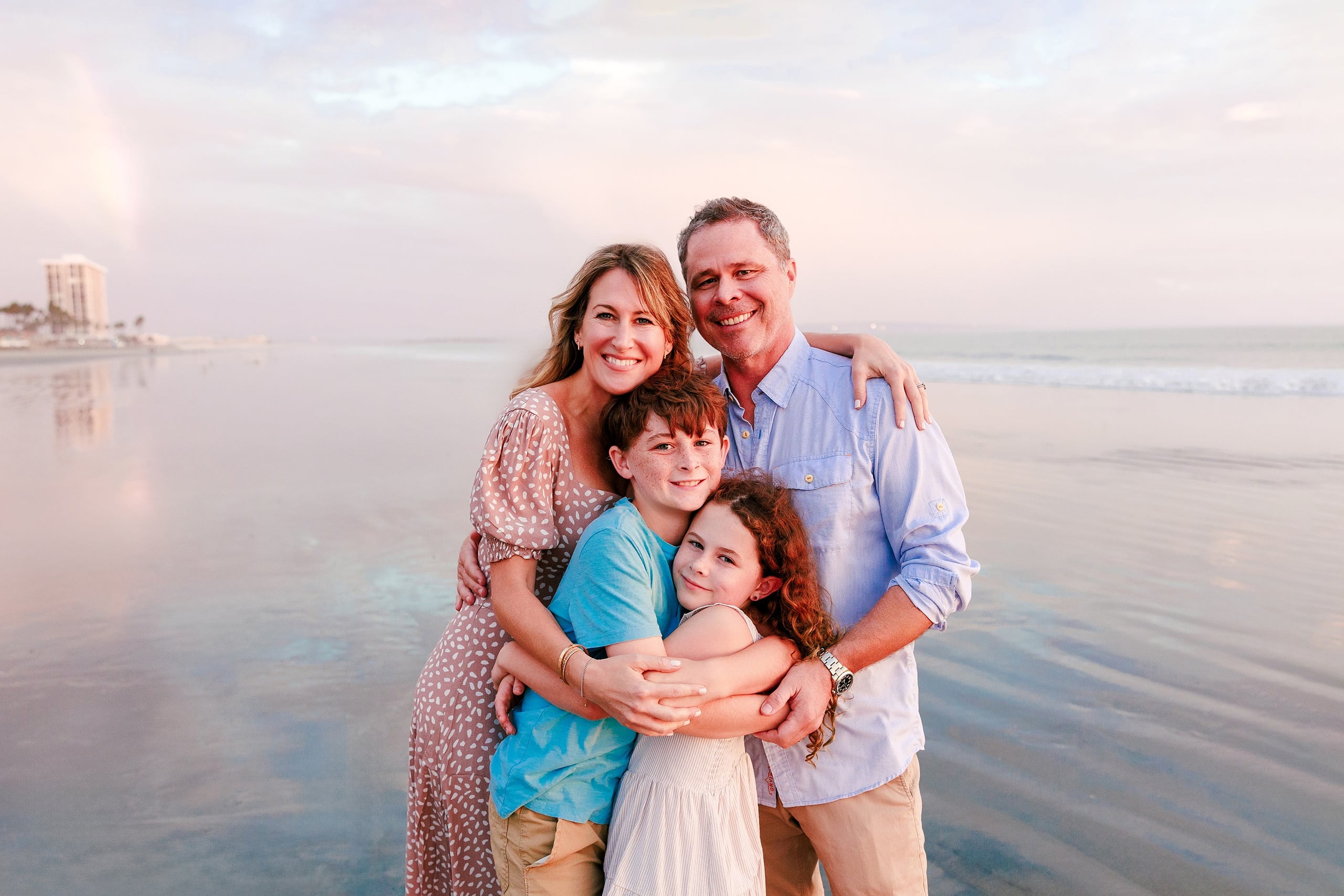 Behind the Scenes of Grammy Judy’s 80th Birthday Session: An Interview with Wendy — 24 Family of four huddled on beach at sunset, silhouetted against pink and golden light