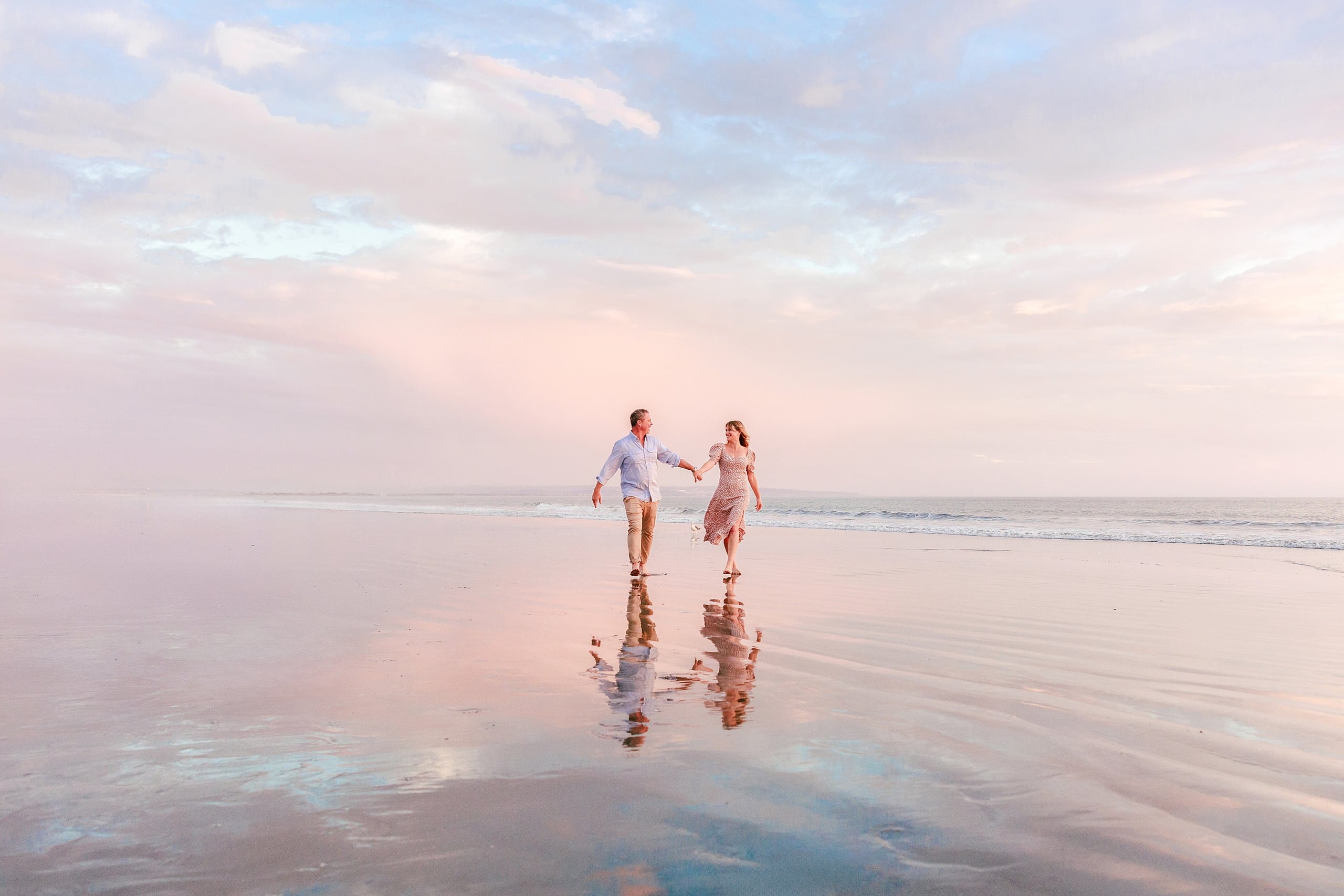 Behind the Scenes of Grammy Judy’s 80th Birthday Session: An Interview with Wendy — 25 Woman and man hold hands, walking together on wet sand at soft golden hour