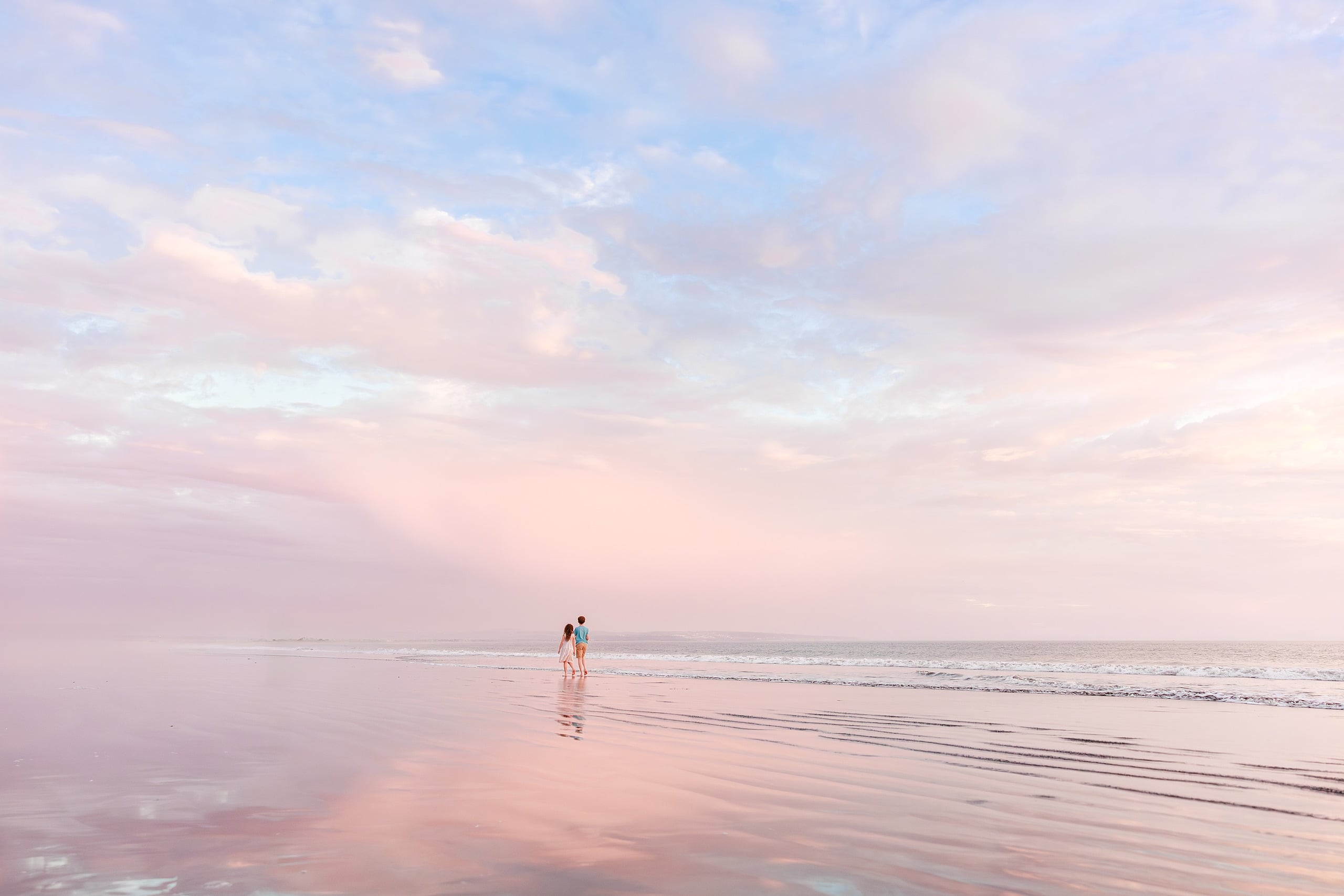Behind the Scenes of Grammy Judy’s 80th Birthday Session: An Interview with Wendy — 27 Couple walking on wet beach sand at soft golden hour, distant view with calm ocean