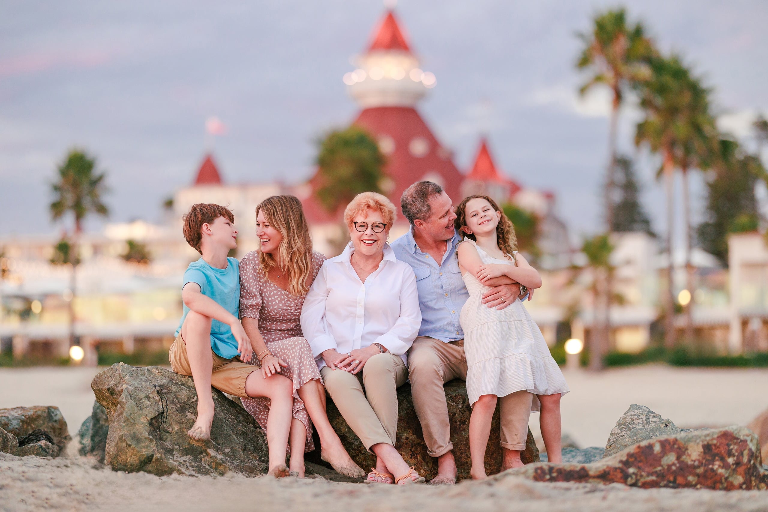 Behind the Scenes of Grammy Judy’s 80th Birthday Session: An Interview with Wendy — 30 Family group of five on rocks on beach with red Hotel del Coronado building in background
