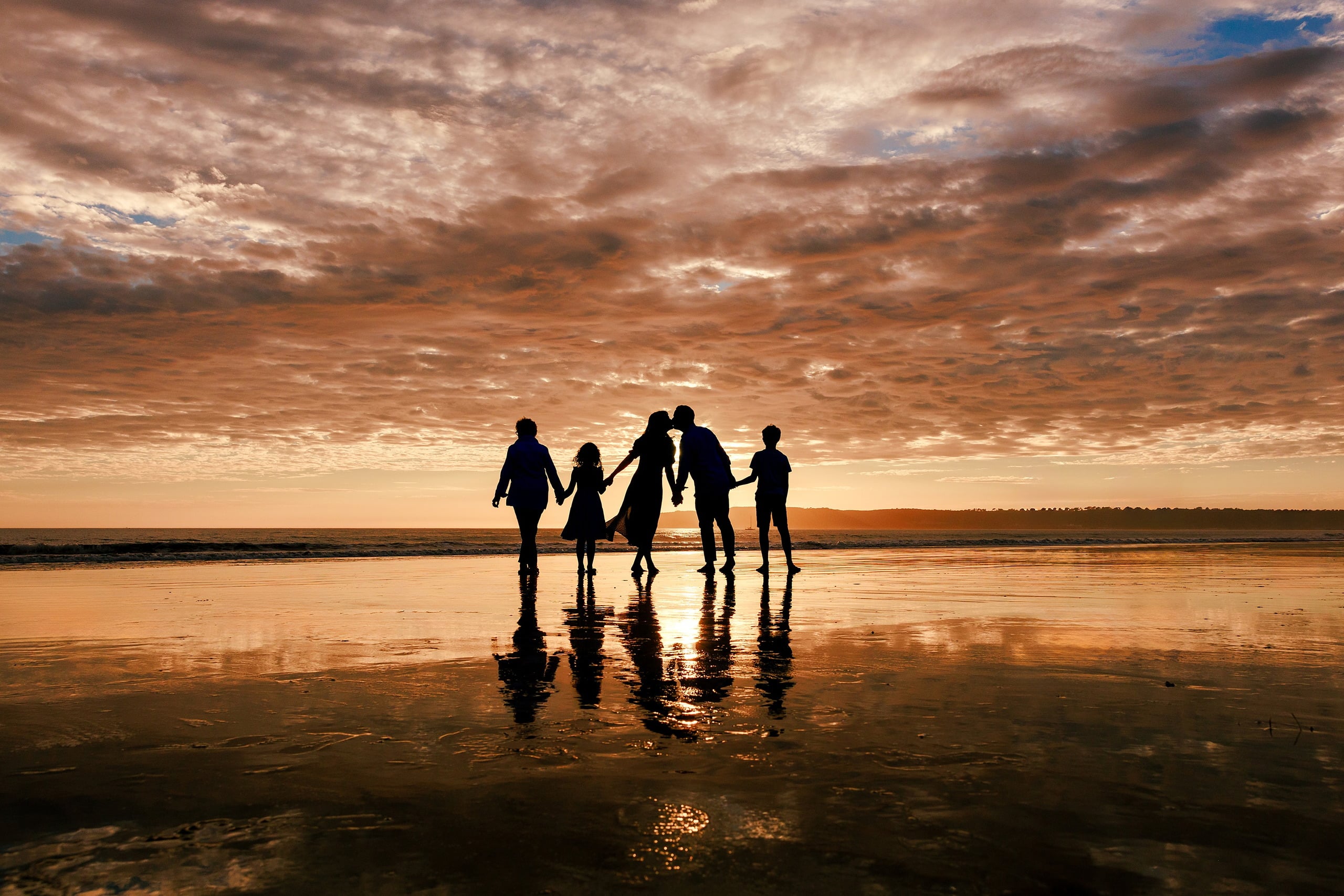 Behind the Scenes of Grammy Judy’s 80th Birthday Session: An Interview with Wendy — 32 Five family members silhouetted hand in hand on wet beach during golden hour sunset