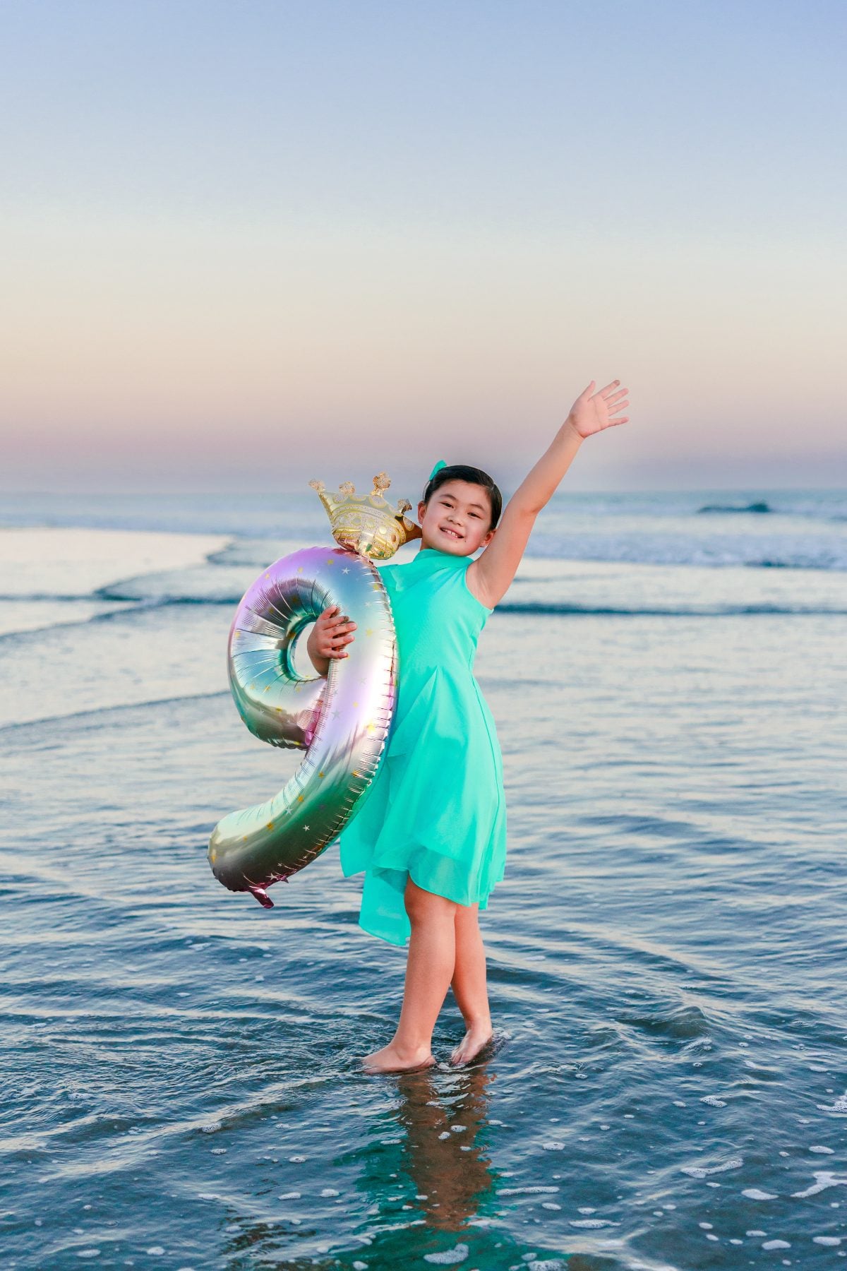 Girl in teal dress celebrates birthday with number balloon on Coronado Beach at sunset