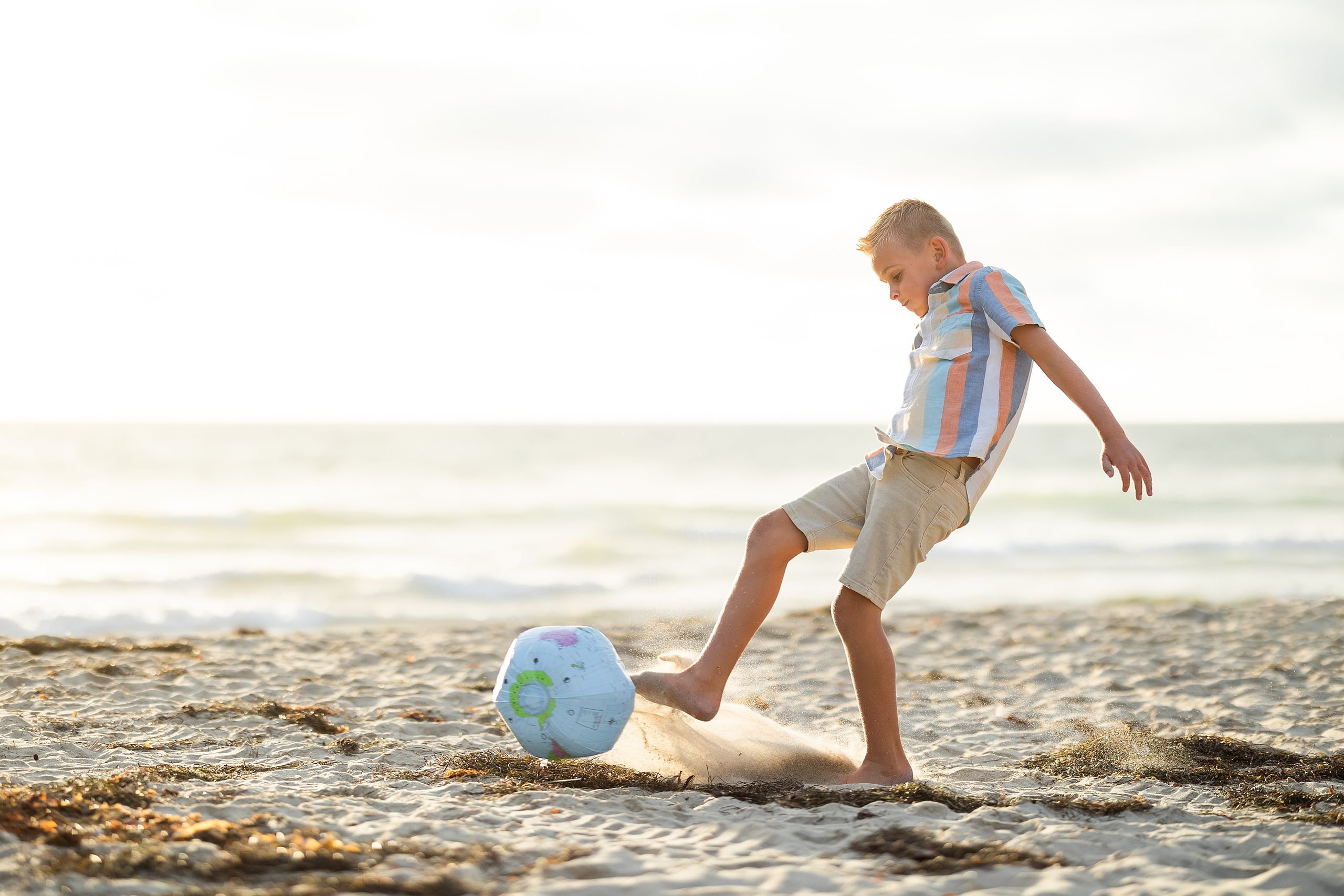 Butlers on the Beach — 08 Child kicking blue and green beach ball on sand near the waterline