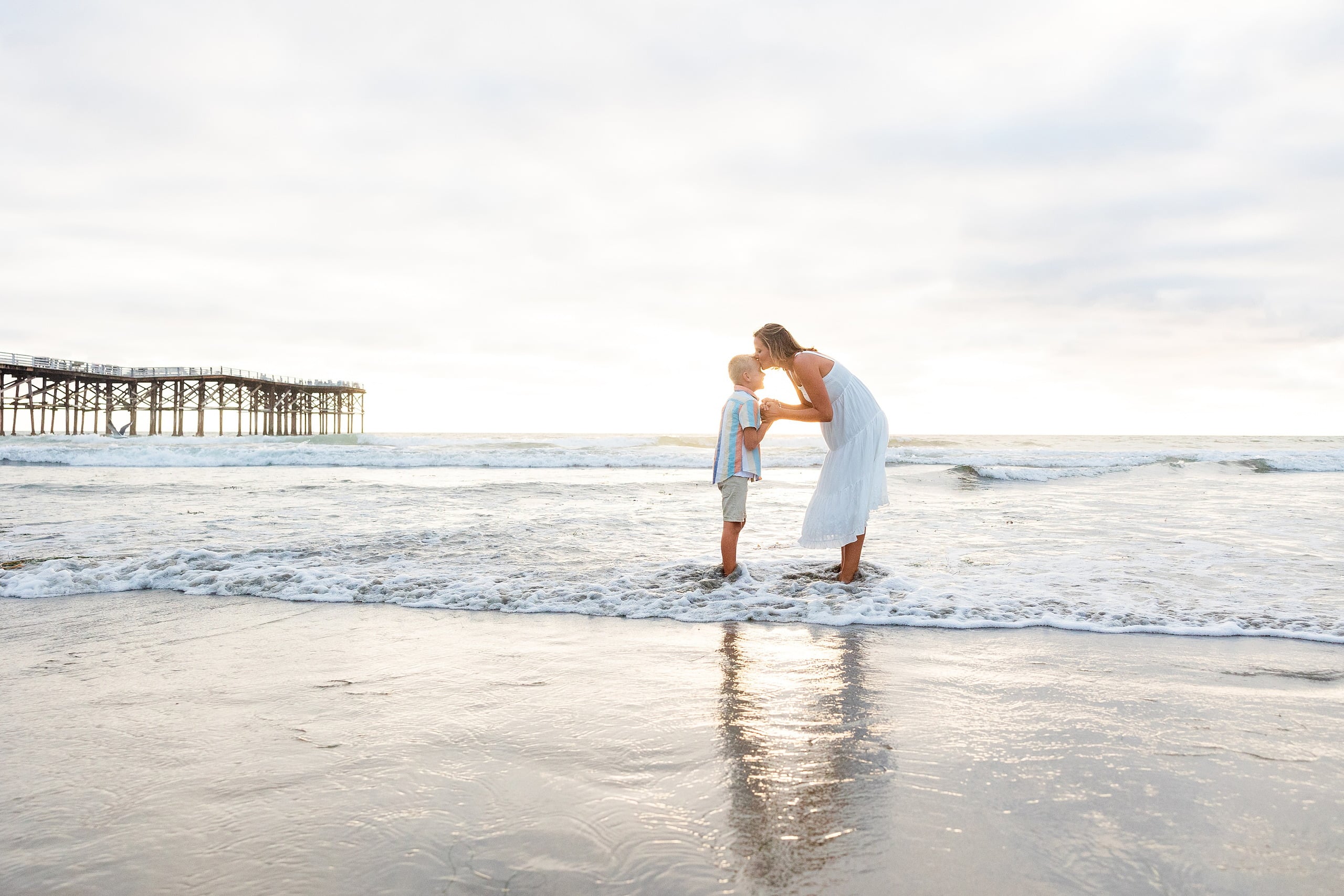 Butlers on the Beach — 12 Woman in white dress bending down to boy's level in shallow water at pier