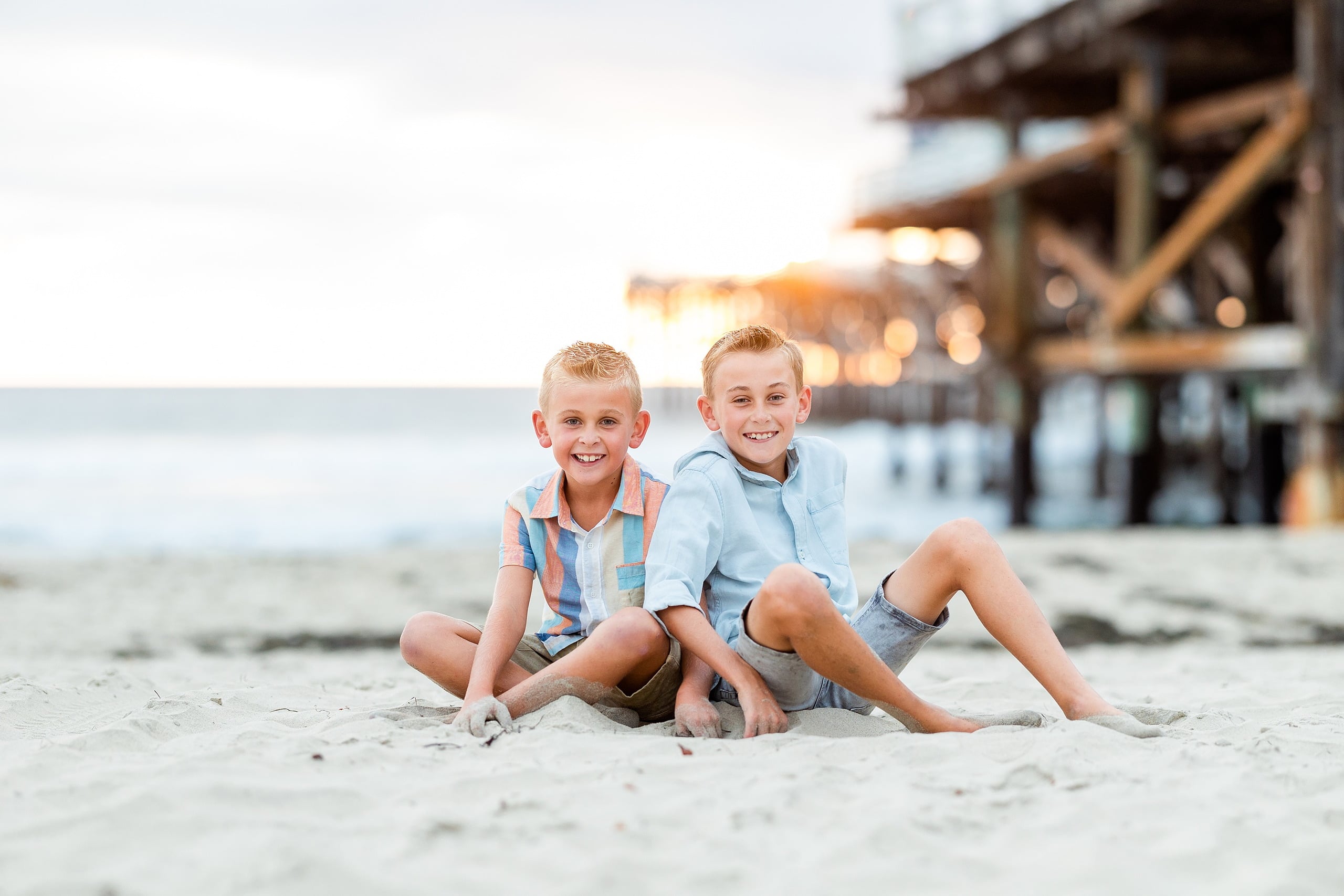 Butlers on the Beach — 23 Two boys sitting together in sand with Crystal Pier pilings behind them