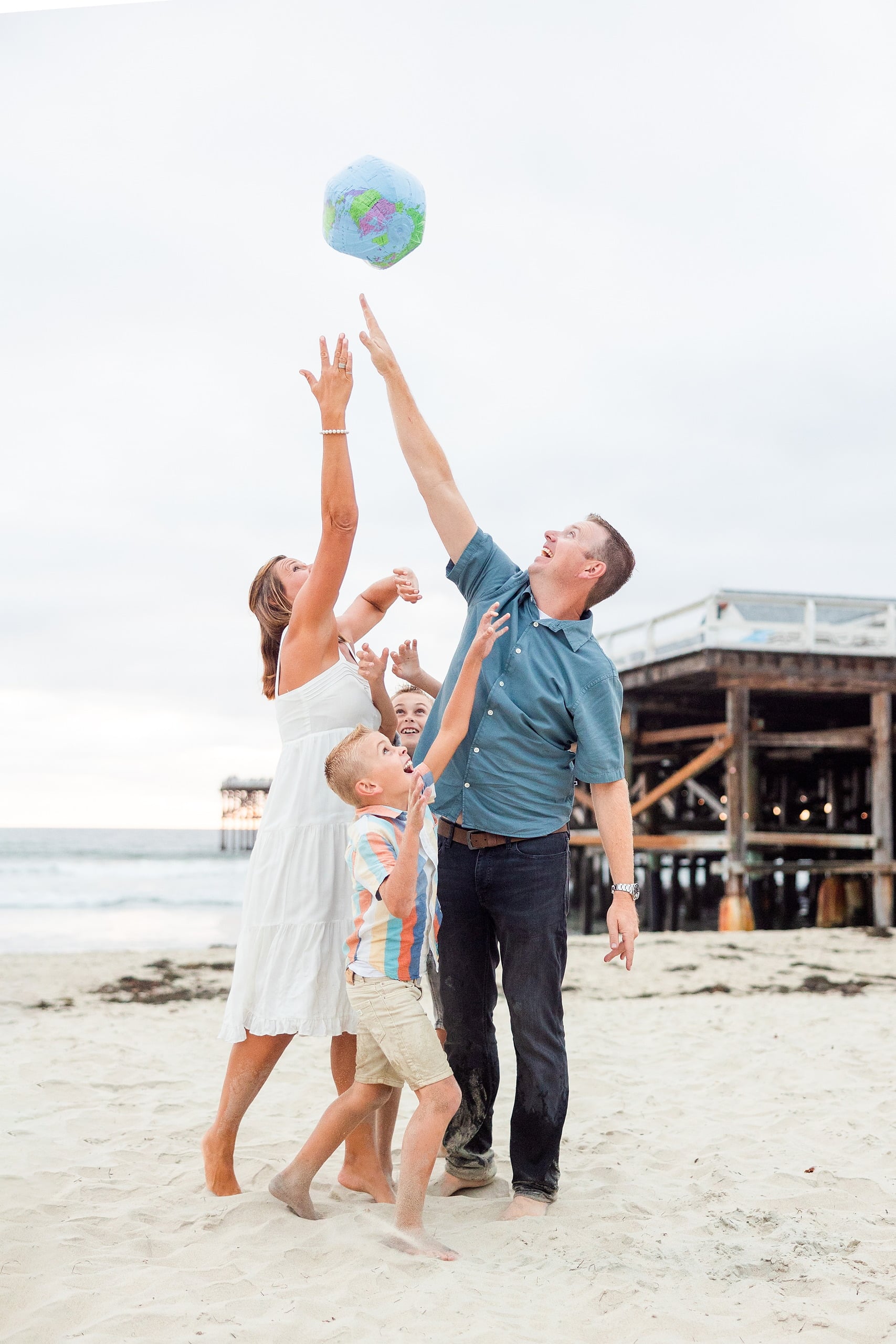 Butlers on the Beach — 25 Family reaching up together to catch and throw colorful beach ball in air at beach