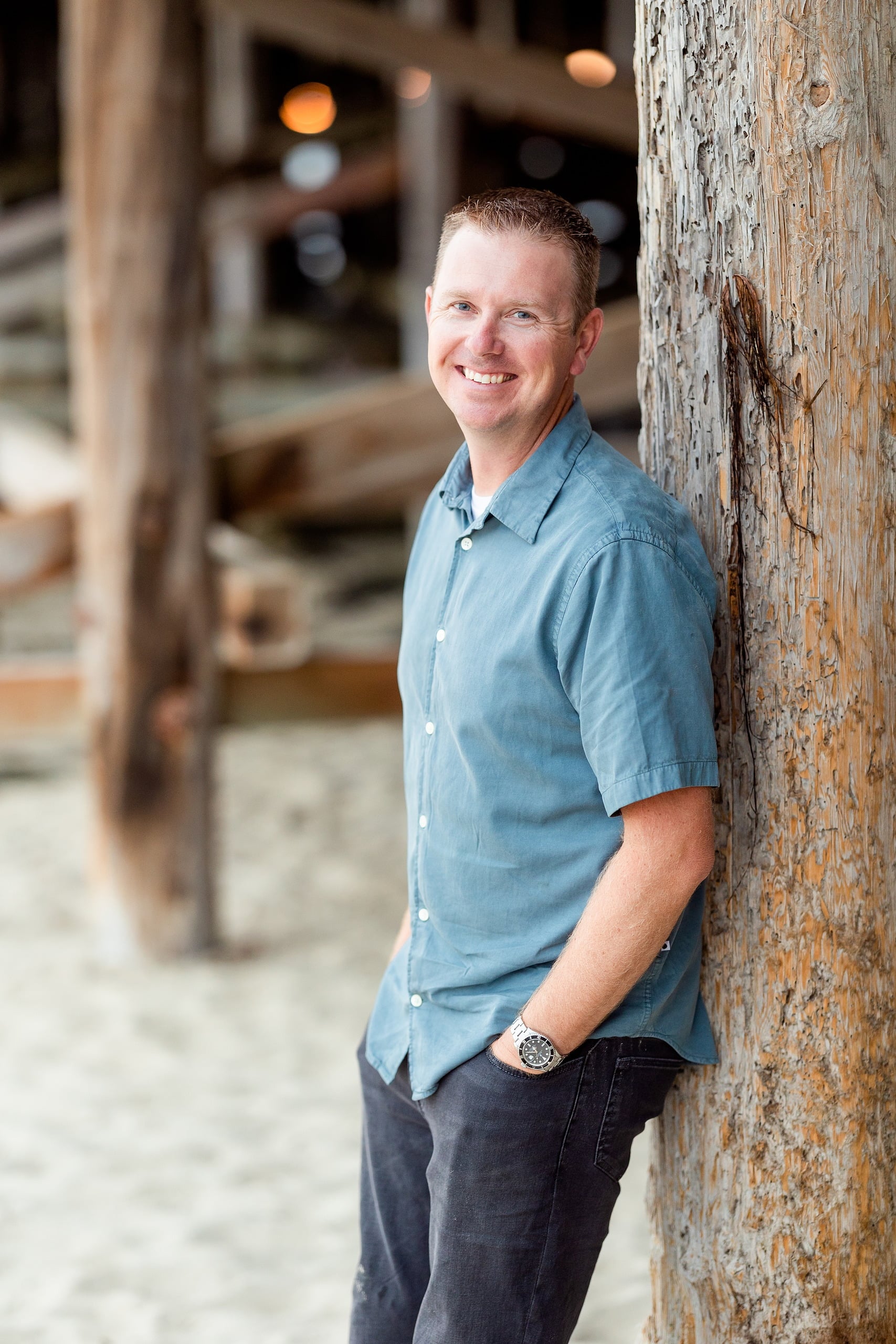 Butlers on the Beach — 26 Man in light blue shirt leaning against weathered wooden pier structure