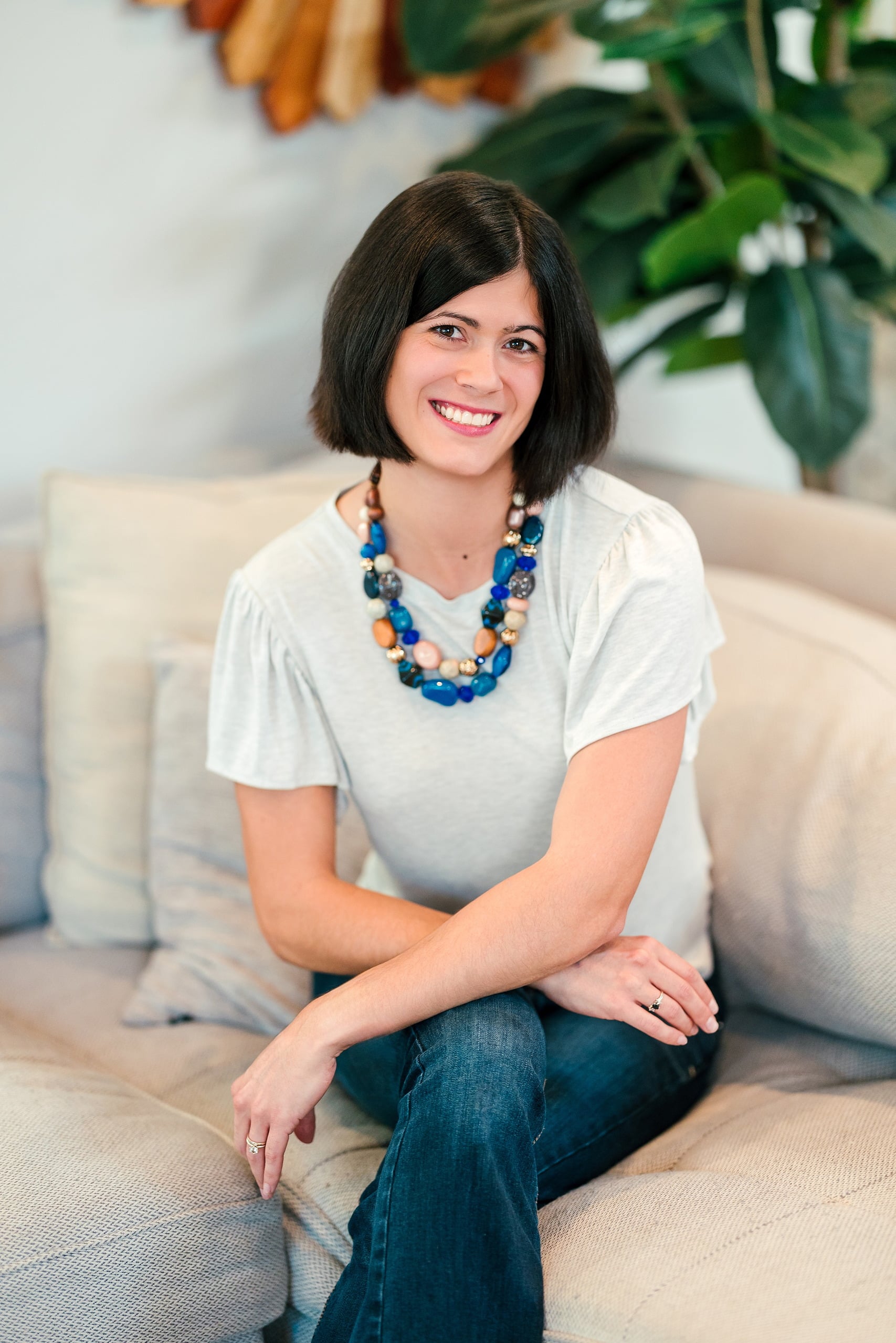 Capturing San Diego Spirit: Intention 2 Impact’s Team Retreat at Windansea — 04 Woman wearing white shirt and blue beaded necklace on cream sofa