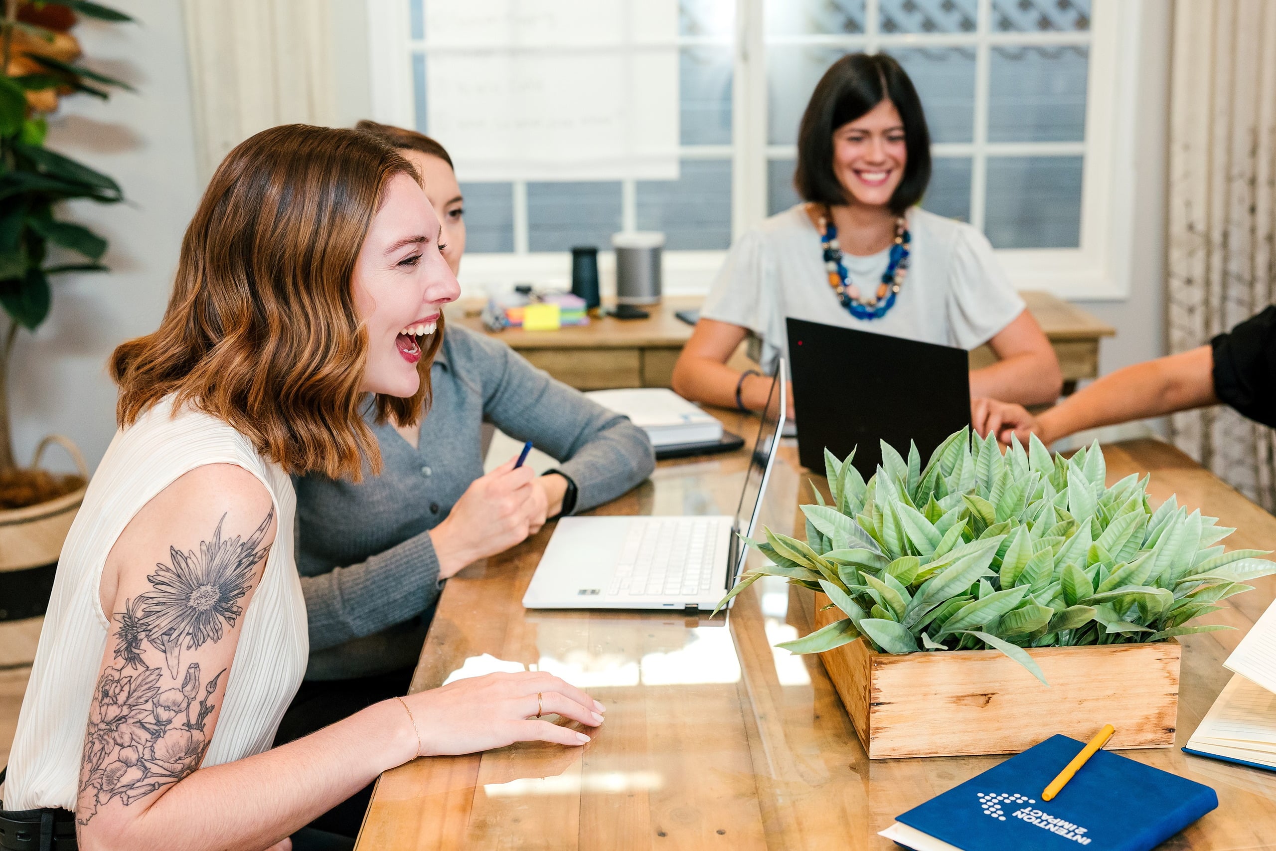 Capturing San Diego Spirit: Intention 2 Impact’s Team Retreat at Windansea — 09 Women at wooden table laughing during work session at La Jolla