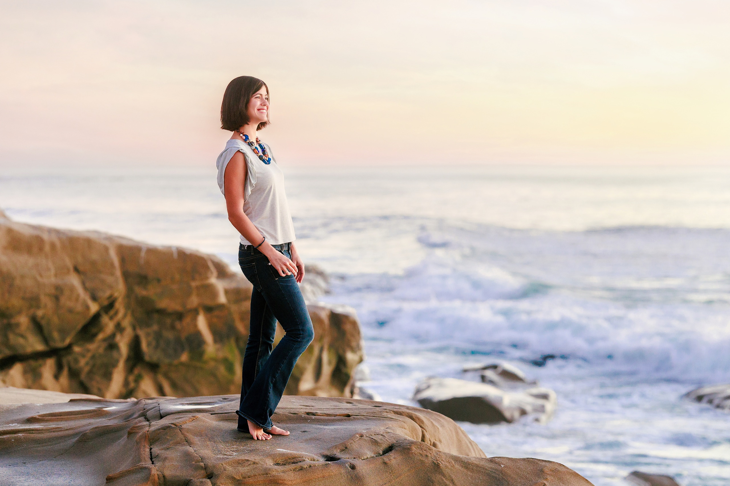 Capturing San Diego Spirit: Intention 2 Impact’s Team Retreat at Windansea — 36 Woman in white shirt standing barefoot on rocky outcrop at sunset