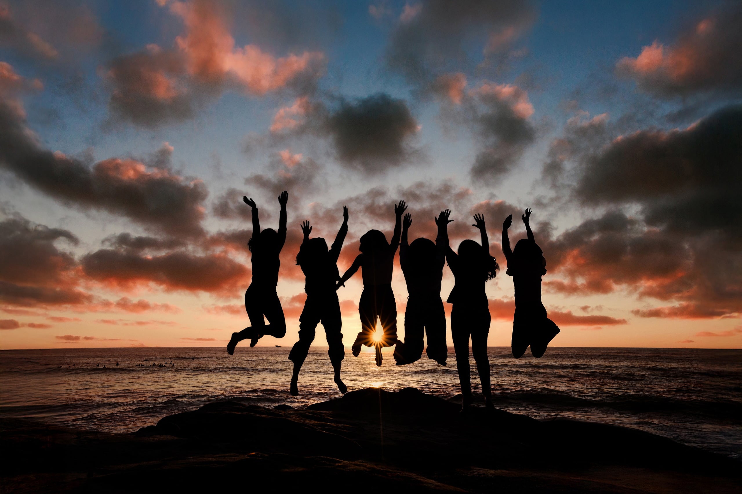 Capturing San Diego Spirit: Intention 2 Impact’s Team Retreat at Windansea — 42 Team in silhouette jumping on Windansea beach at vibrant golden hour