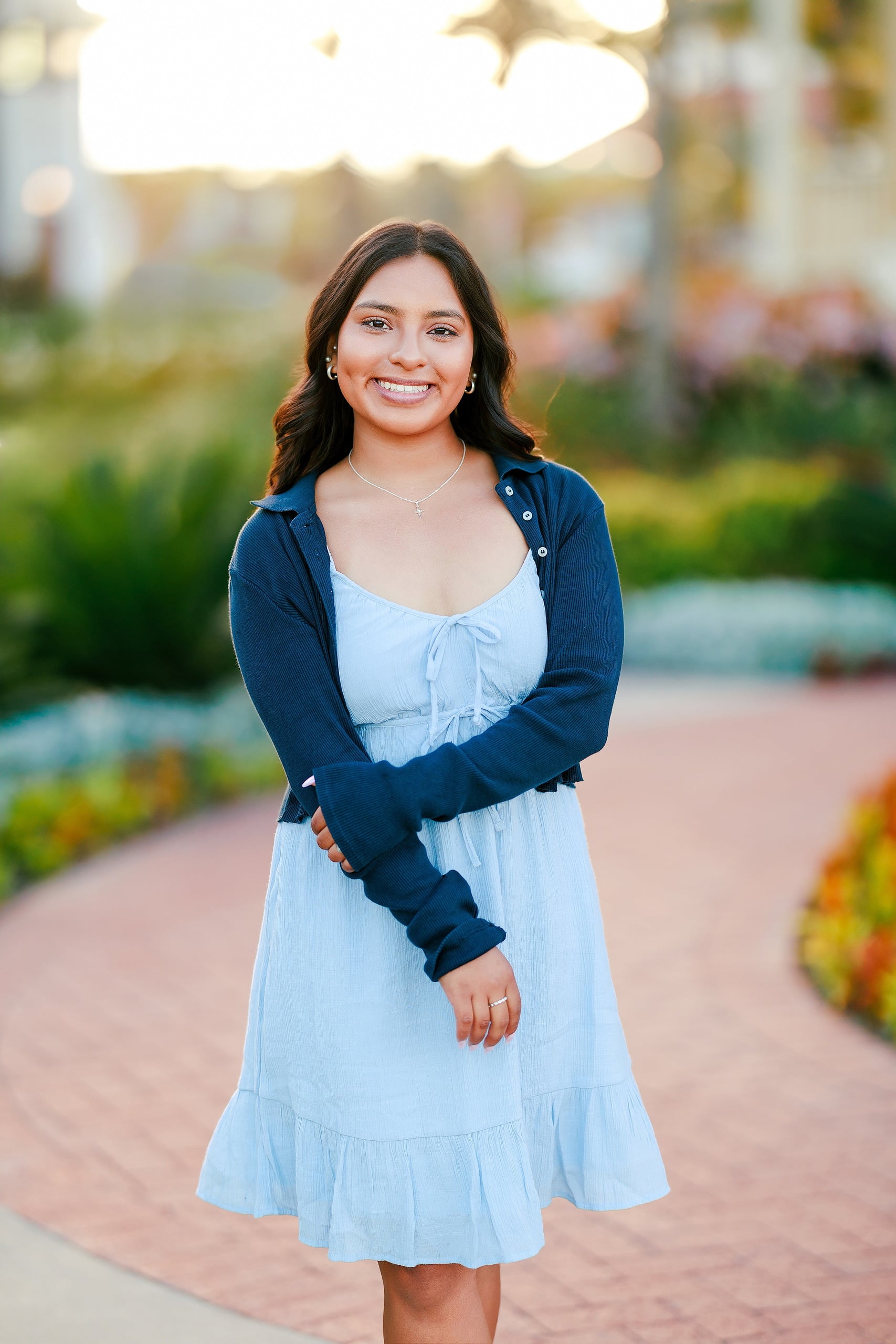 Evanna, Atalia, and Erleen’s Senior Session on Coronado — 05 Senior in light blue dress kneeling on brick path at Hotel del Coronado
