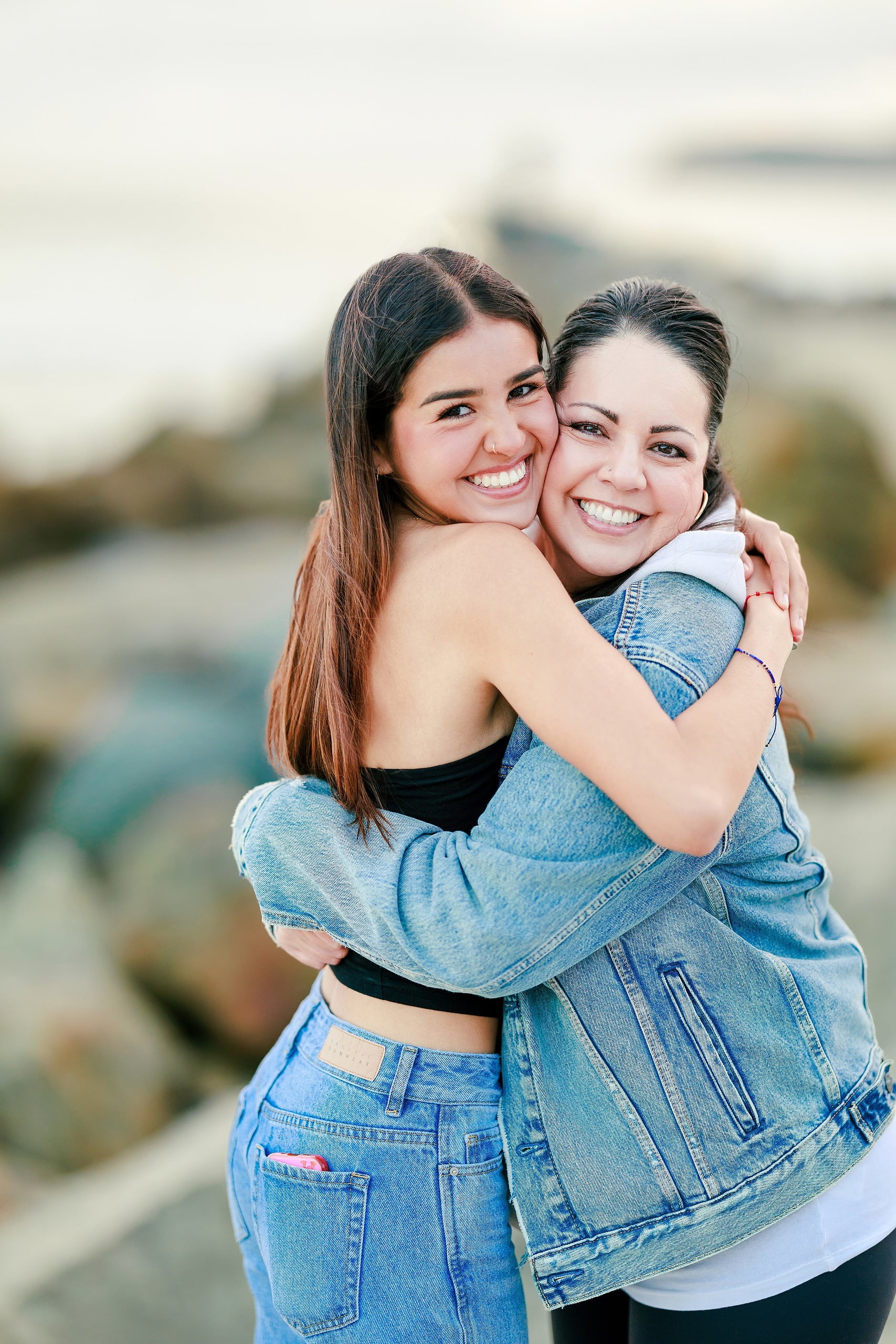 Evanna, Atalia, and Erleen’s Senior Session on Coronado — 19 Two seniors hugging on beach with pier visible at Coronado