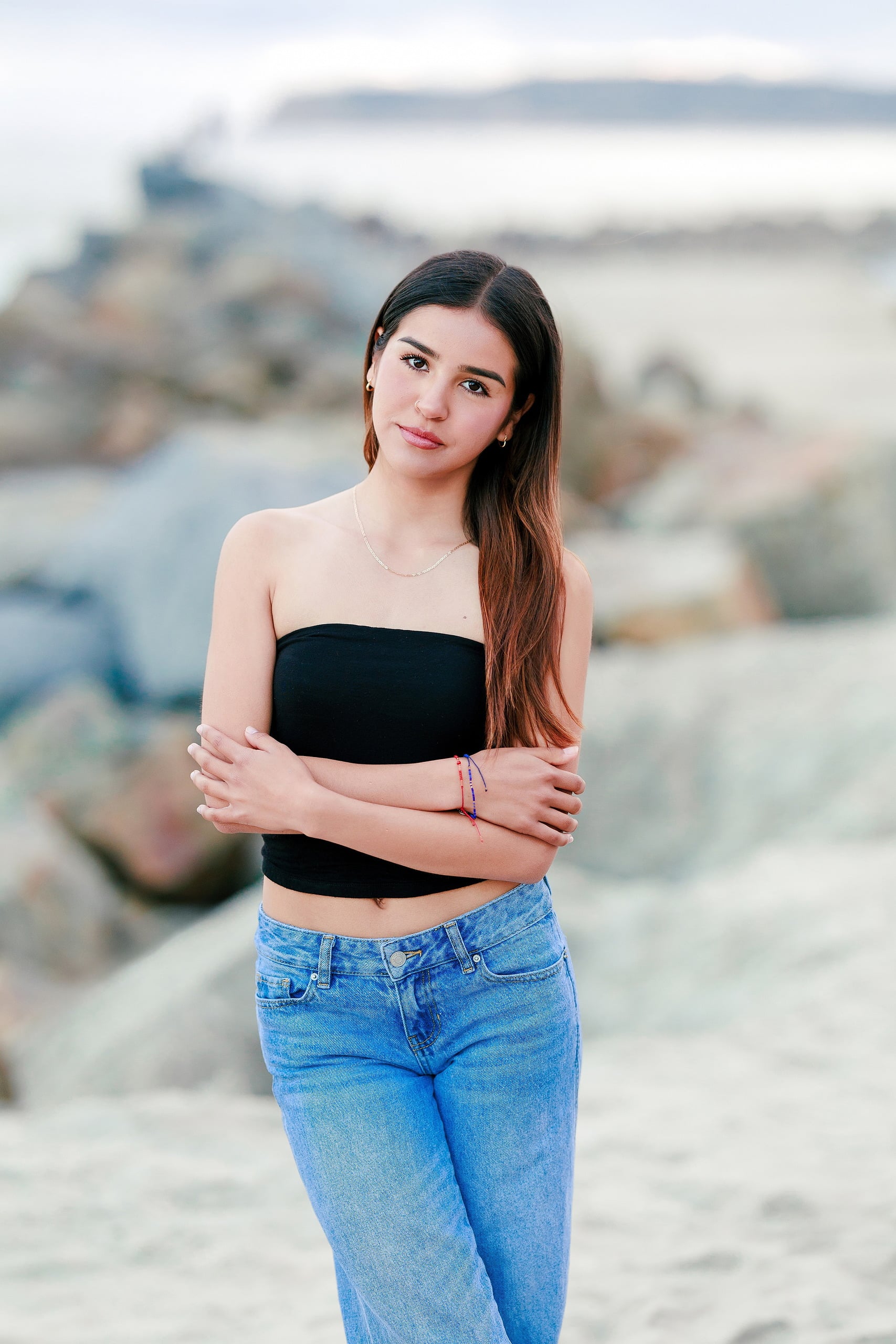 Evanna, Atalia, and Erleen’s Senior Session on Coronado — 21 Senior in black crop top and jeans on sand by rocks at Coronado