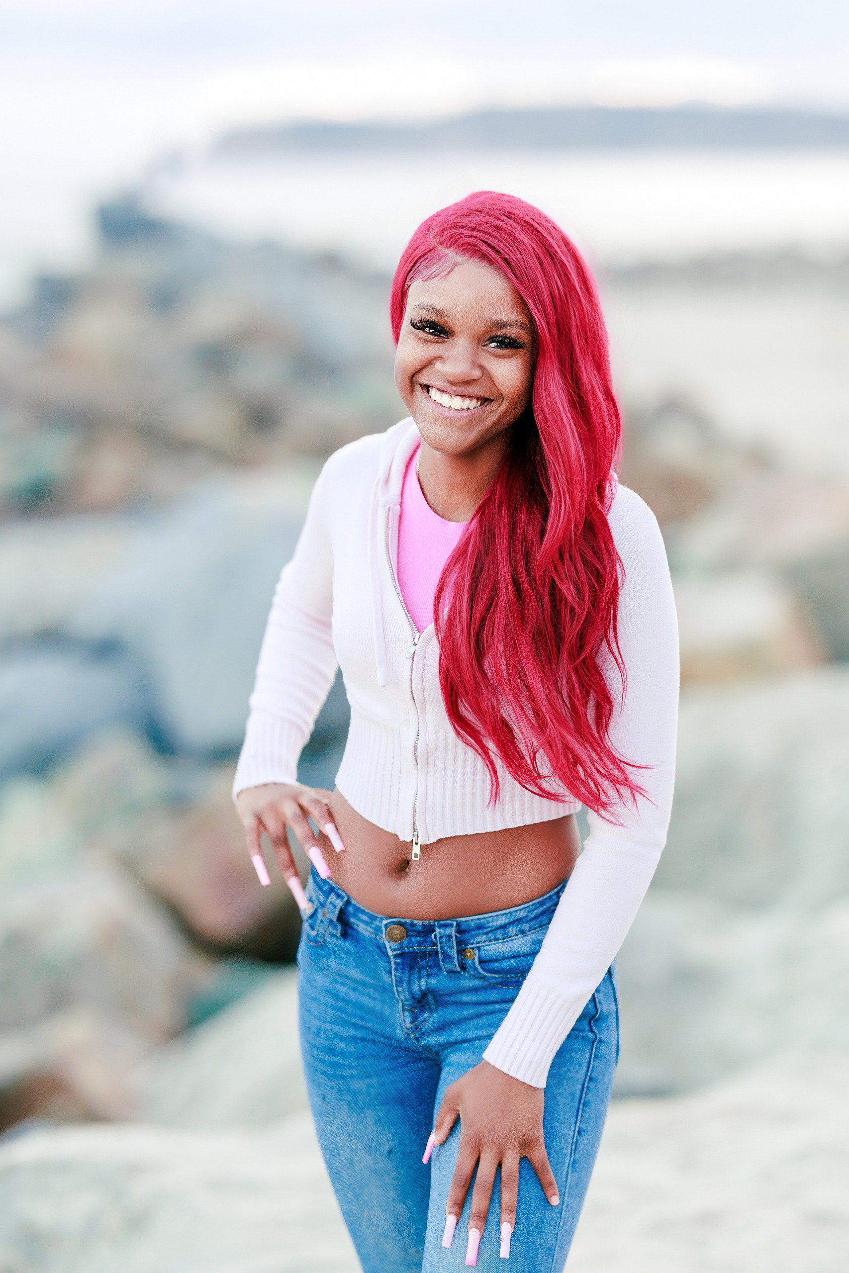 Evanna, Atalia, and Erleen’s Senior Session on Coronado — 22 Senior with pink hair in white crop top smiling on Coronado beach