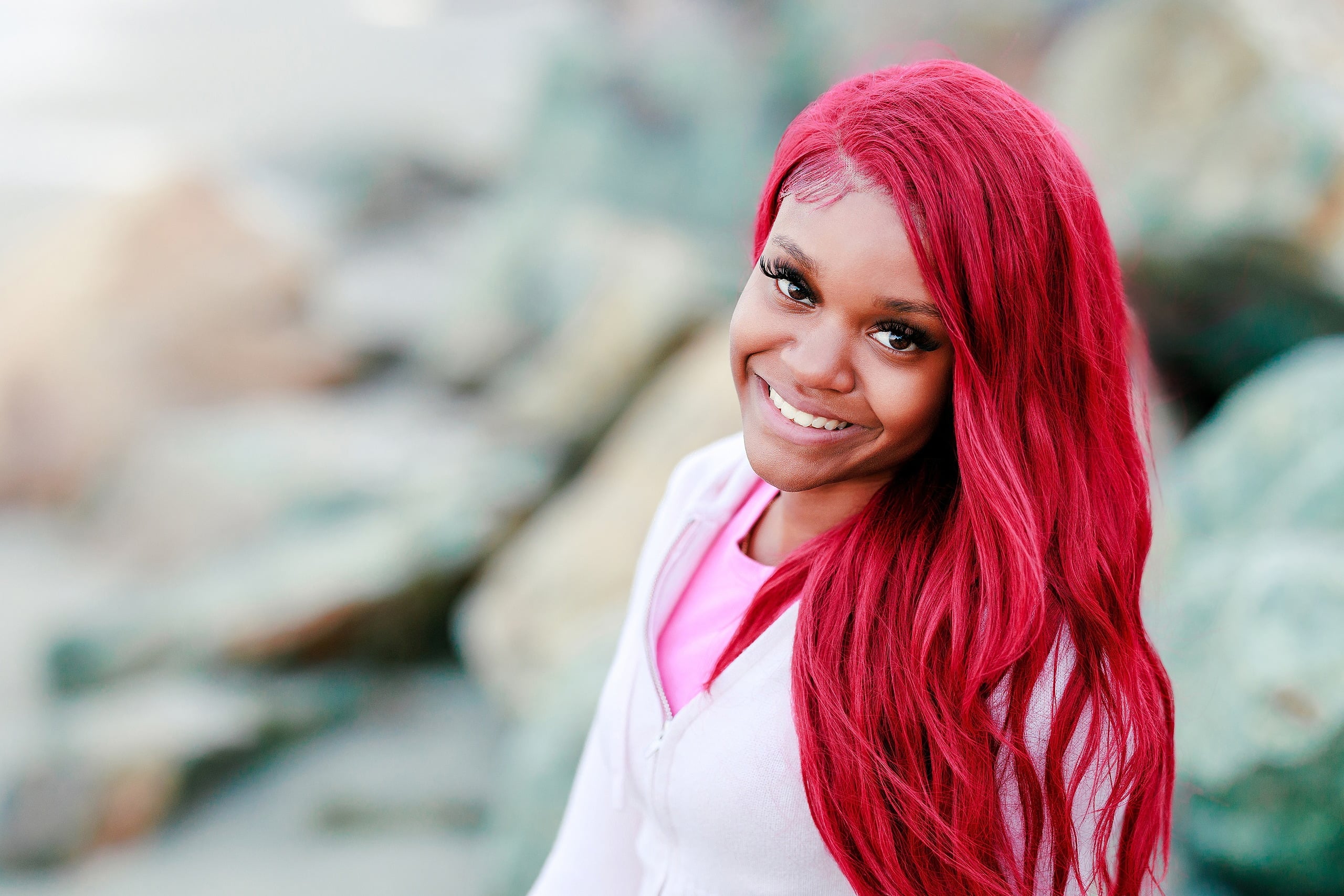 Evanna, Atalia, and Erleen’s Senior Session on Coronado — 26 Senior with pink hair smiling on painted rocks at Coronado shore