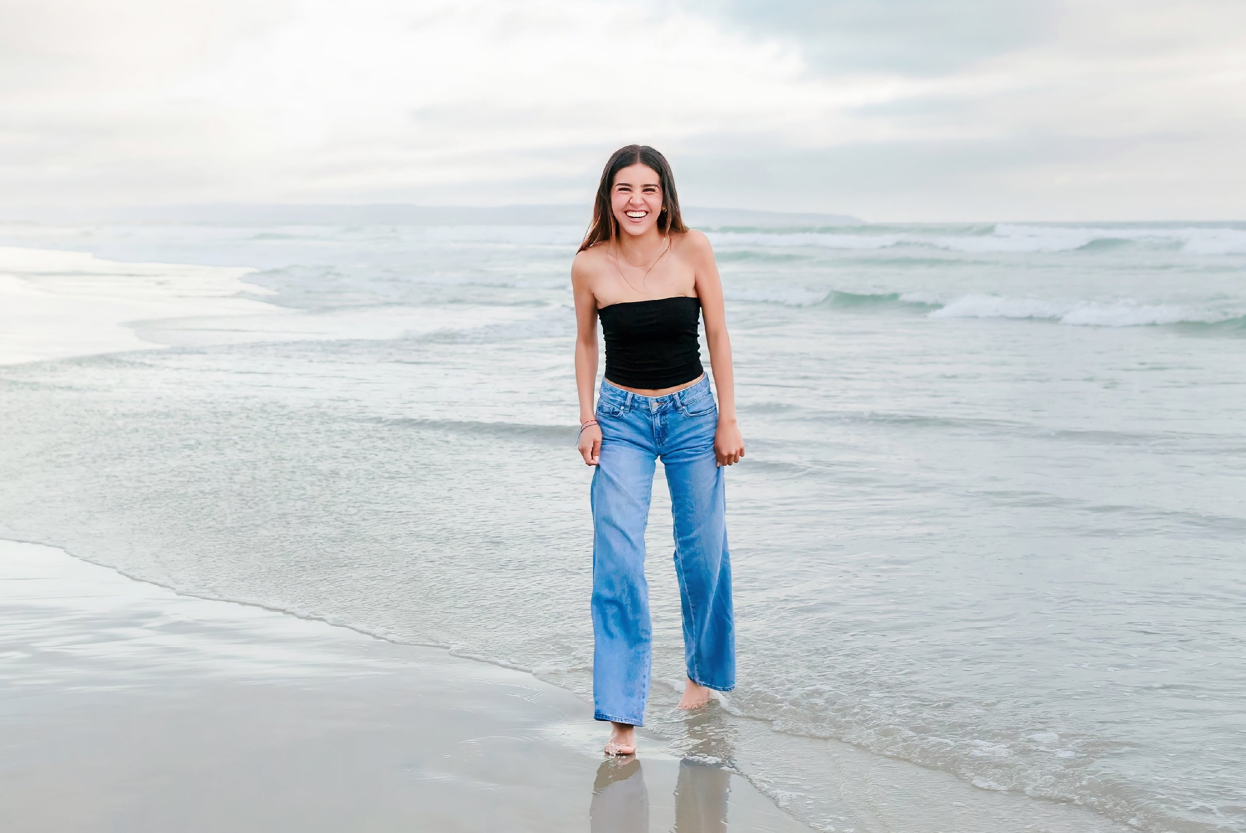 Evanna, Atalia, and Erleen’s Senior Session on Coronado — 31 Senior in black crop top wading in ocean waves at Coronado