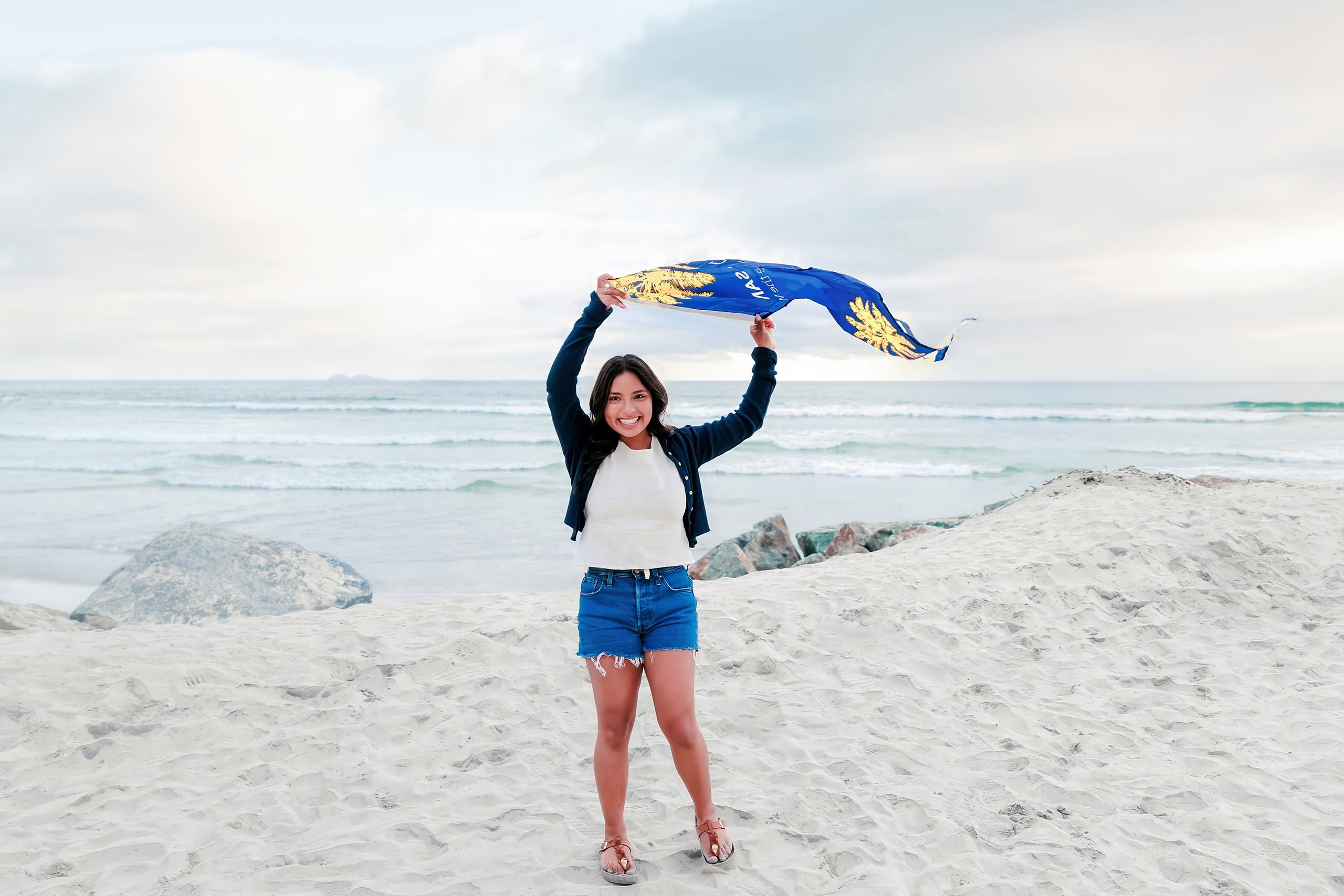 Evanna, Atalia, and Erleen’s Senior Session on Coronado — 36 Senior holding UC Santa Barbara banner on sand by ocean at Coronado