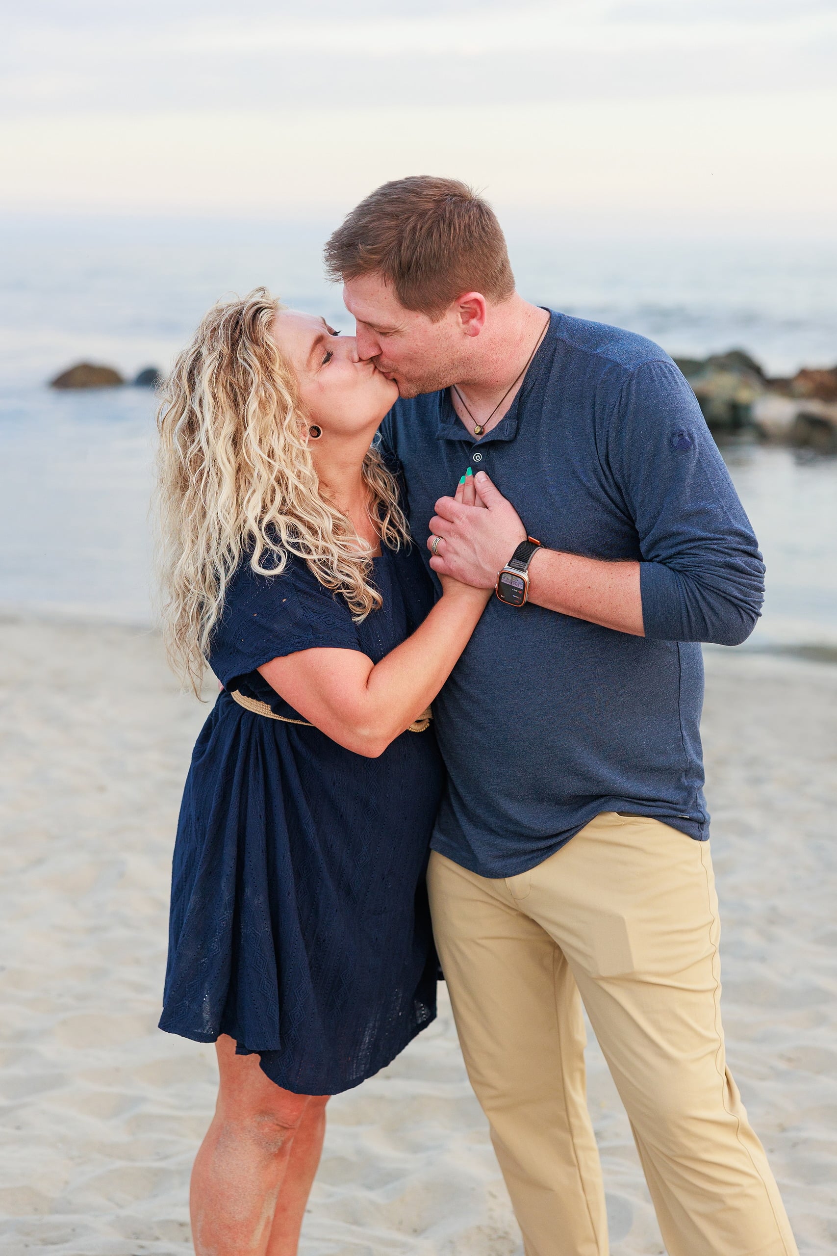 Extended Family Photography Hotel Del Coronado — 04 Man and woman kiss affectionately on Coronado beach, rocky shore visible
