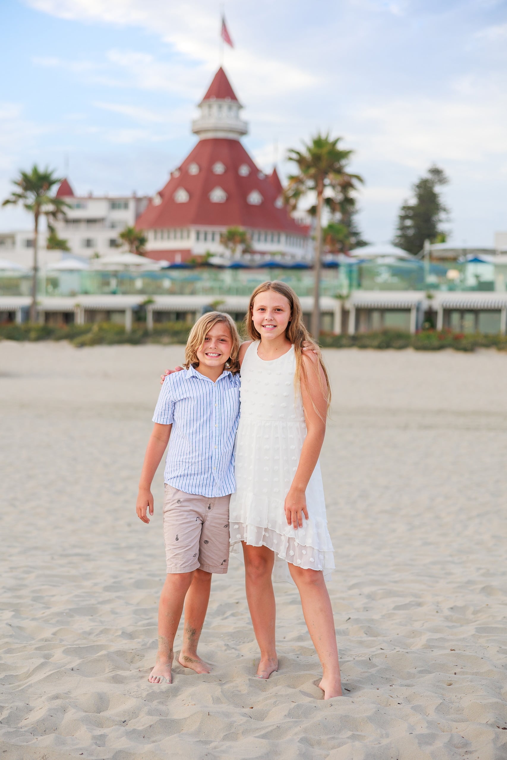 Extended Family Photography Hotel Del Coronado — 05 Two children stand barefoot on sand smiling toward Hotel del Coronado