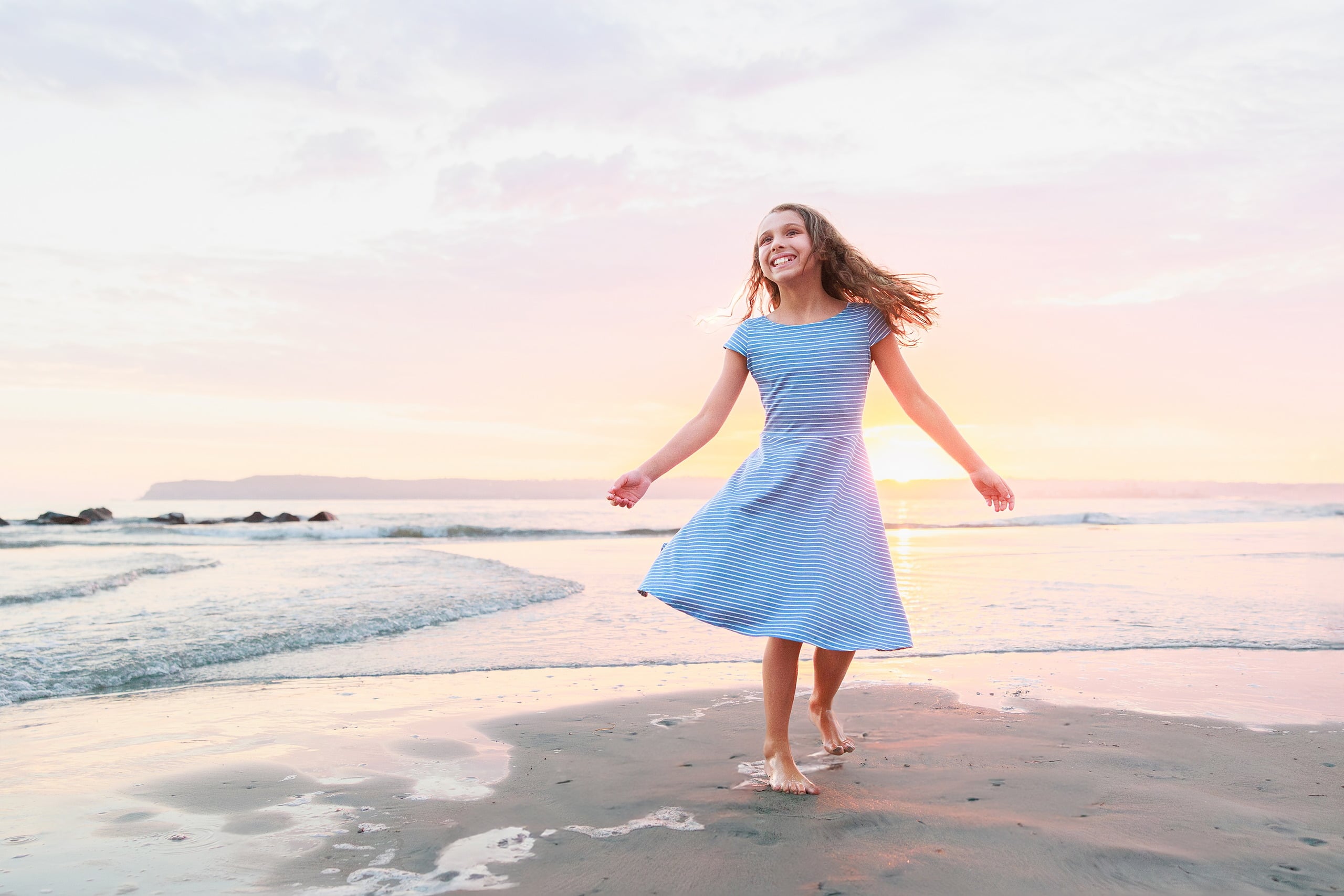 Extended Family Photography Hotel Del Coronado — 11 Teen girl in striped blue dress runs across wet sand at sunset