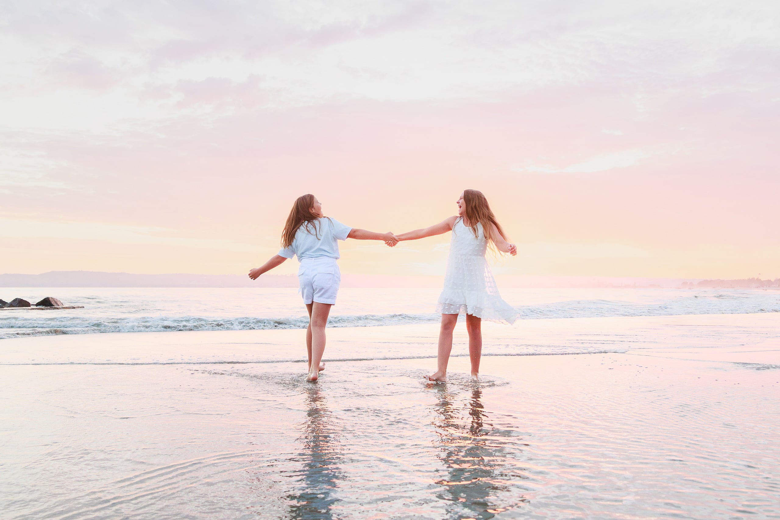 Extended Family Photography Hotel Del Coronado — 12 Two girls hold hands wading in shallow ocean water at golden hour