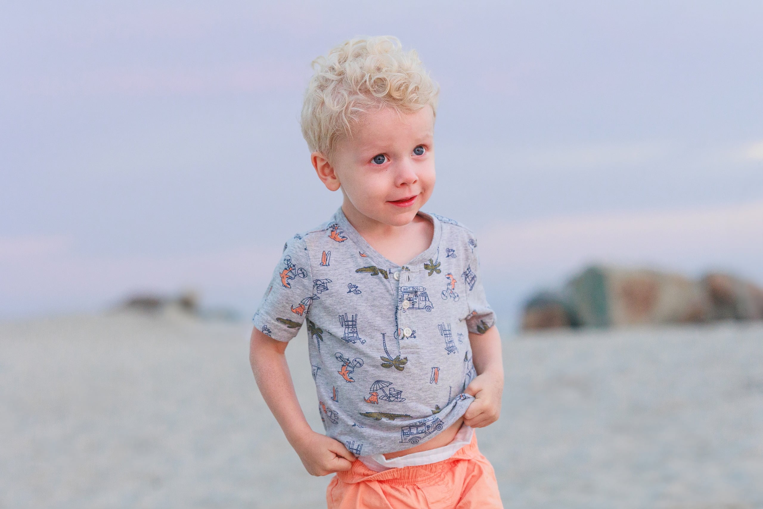 Extended Family Photography Hotel Del Coronado — 21 Young toddler in patterned shirt stands on sand near the ocean