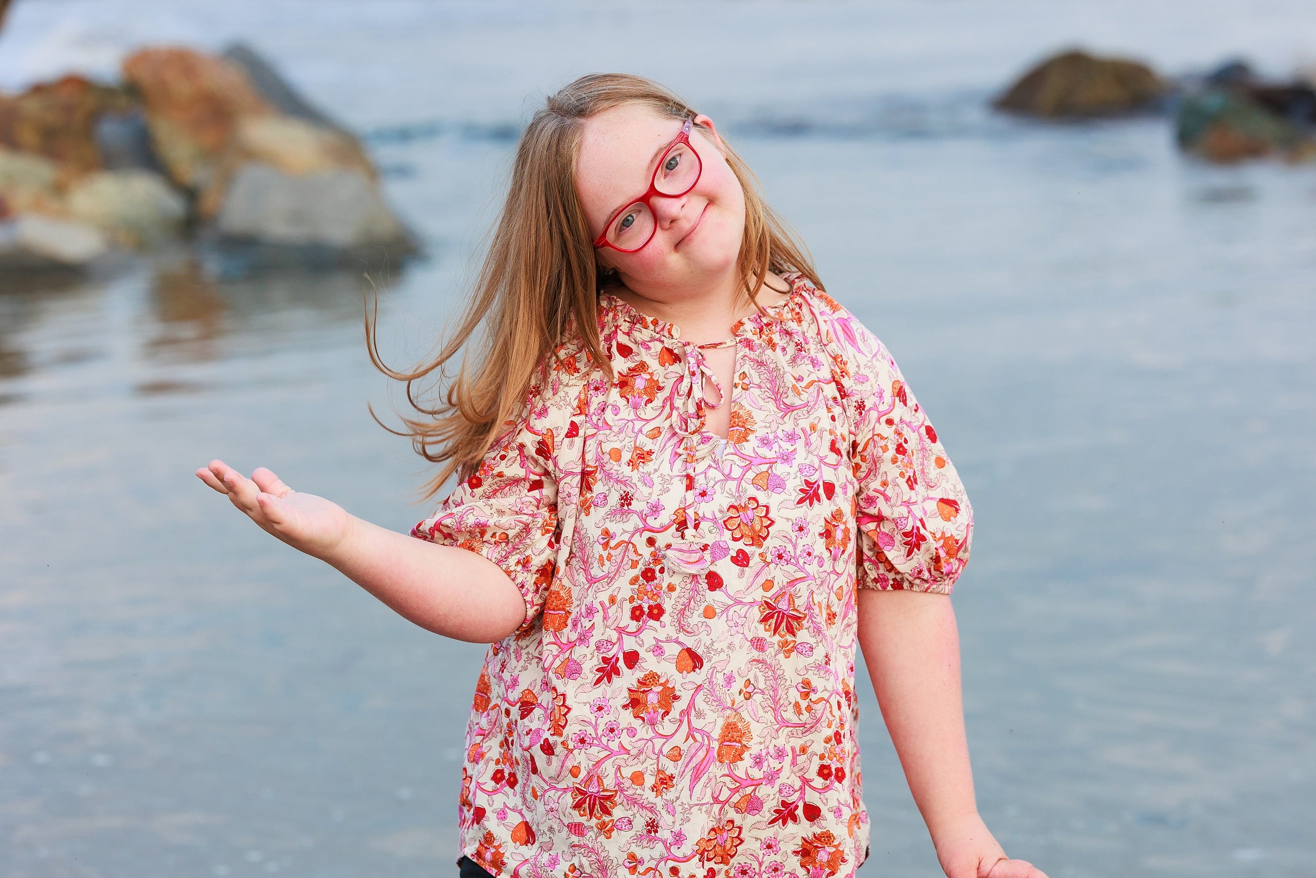 Extended Family Photography Hotel Del Coronado — 26 Child in pink floral shirt stands on rocky beach with arms raised happily