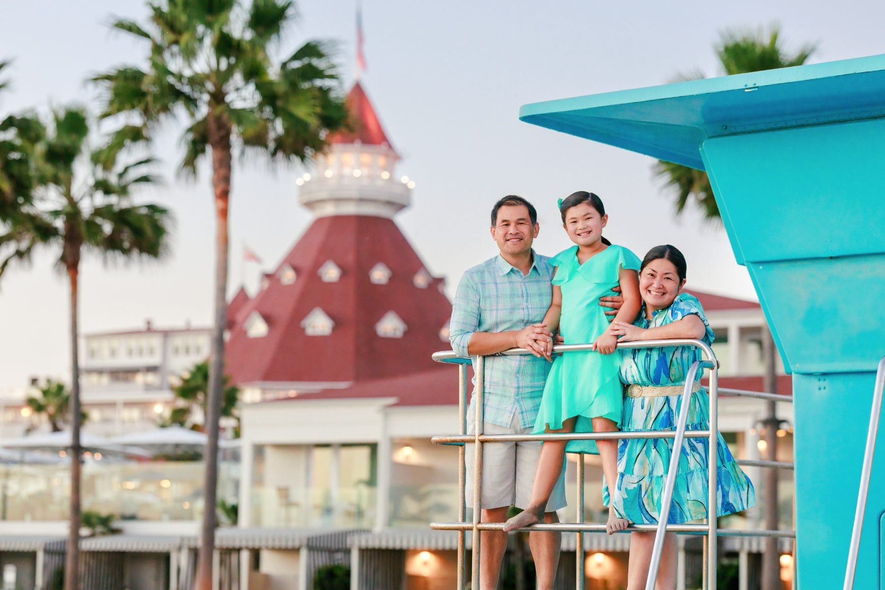 Family of three on lifeguard tower with Hotel Del Coronado behind them