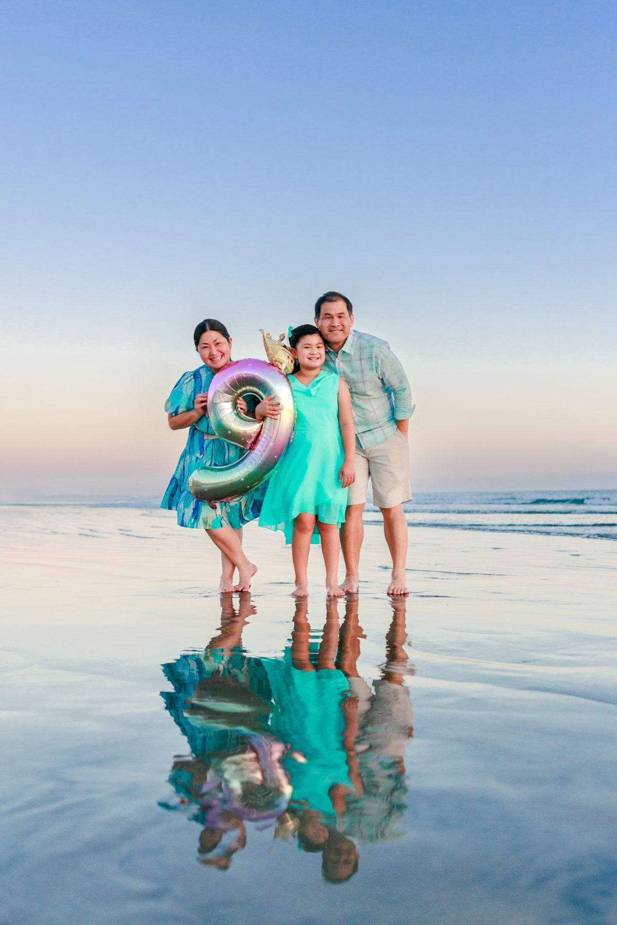 Family of three holding a pool float on Coronado Beach at dusk