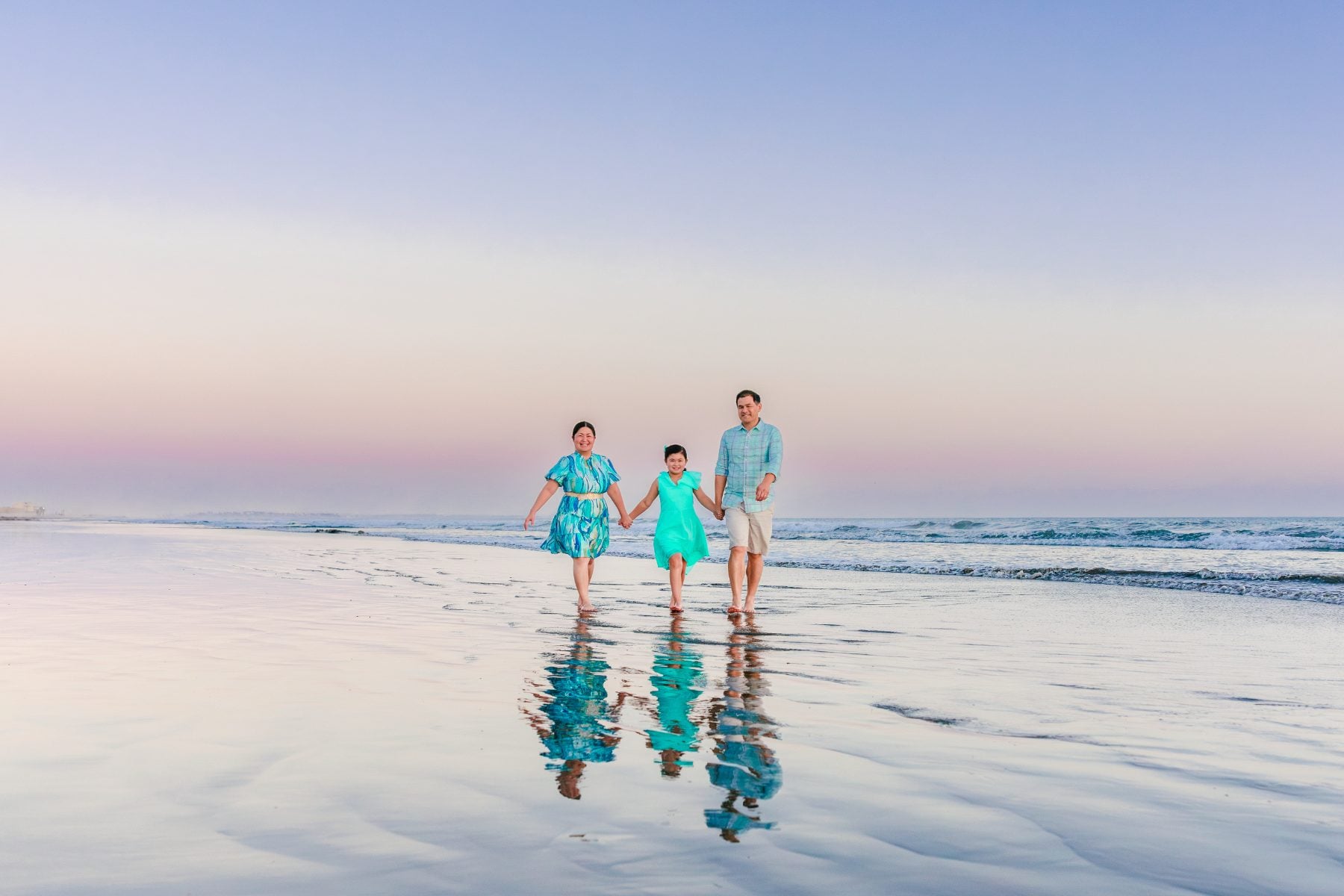 Family of three walks along Coronado beach reflected in wet sand