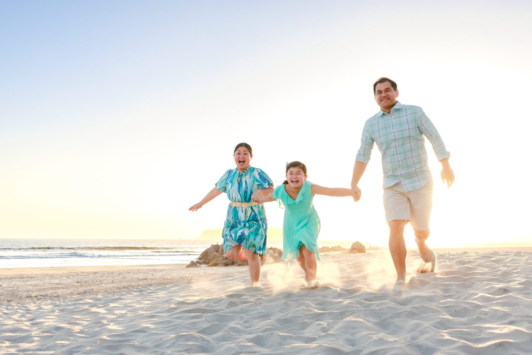 Father runs on the sand with two laughing kids at sunrise