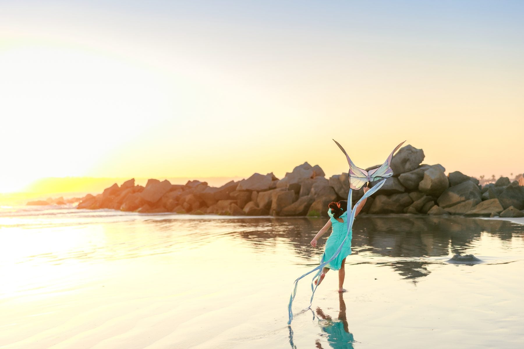Girl running with butterfly kite along Coronado Beach at sunset, back view
