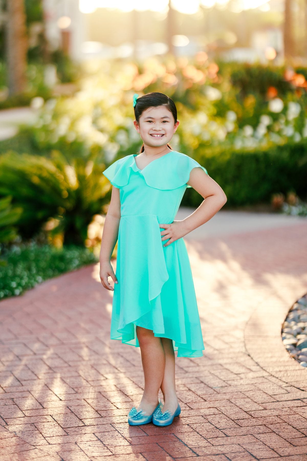 Girl in turquoise dress posing hand on hip on brick garden path