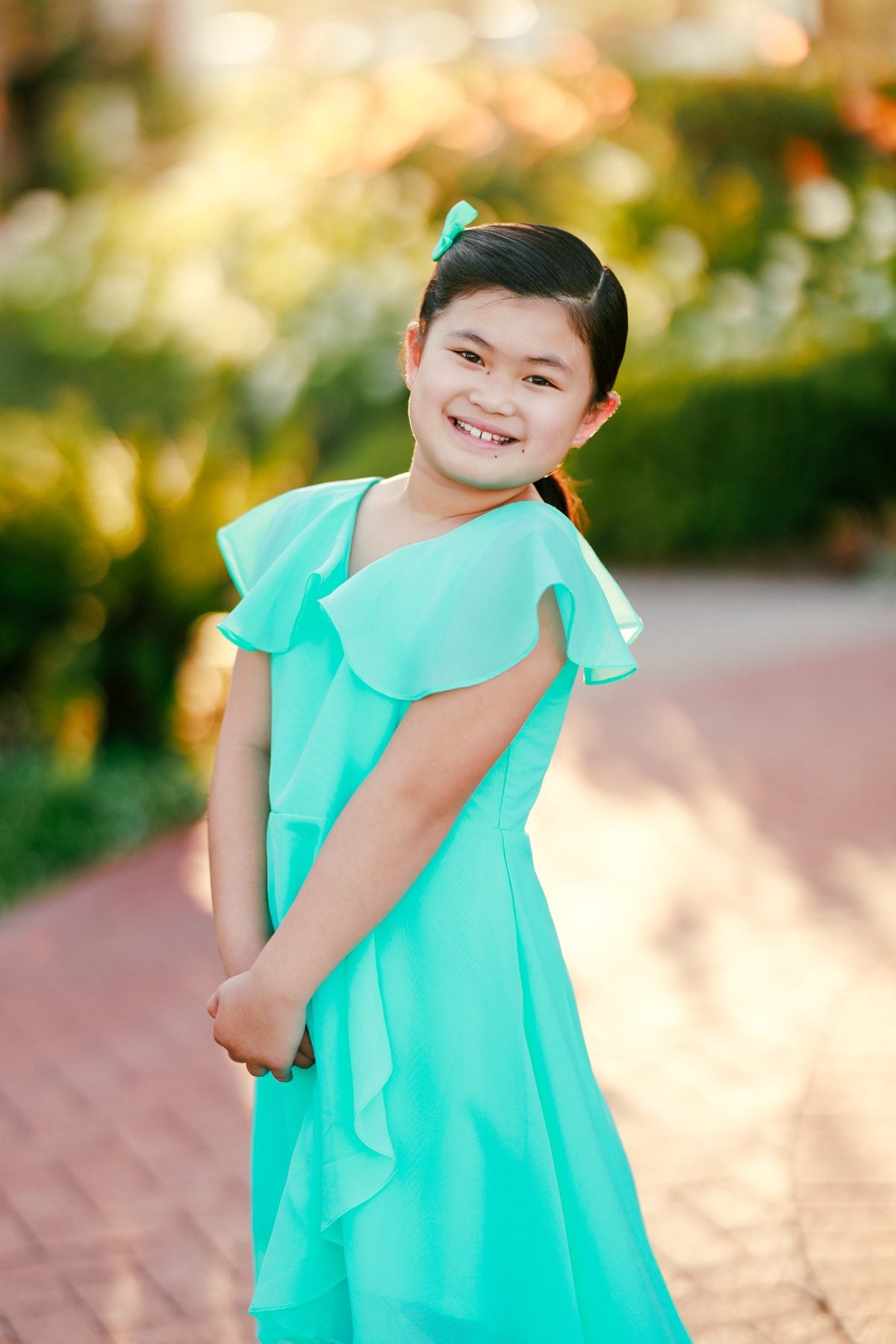 Girl in turquoise dress smiling back over her shoulder on path