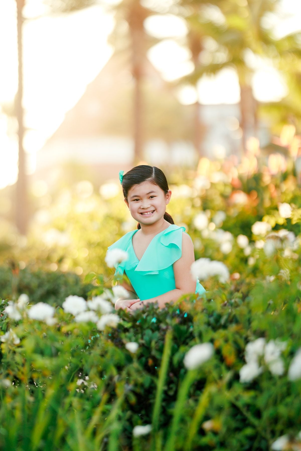 Girl in teal dress sitting among white blooms and palm trees at Hotel del Coronado
