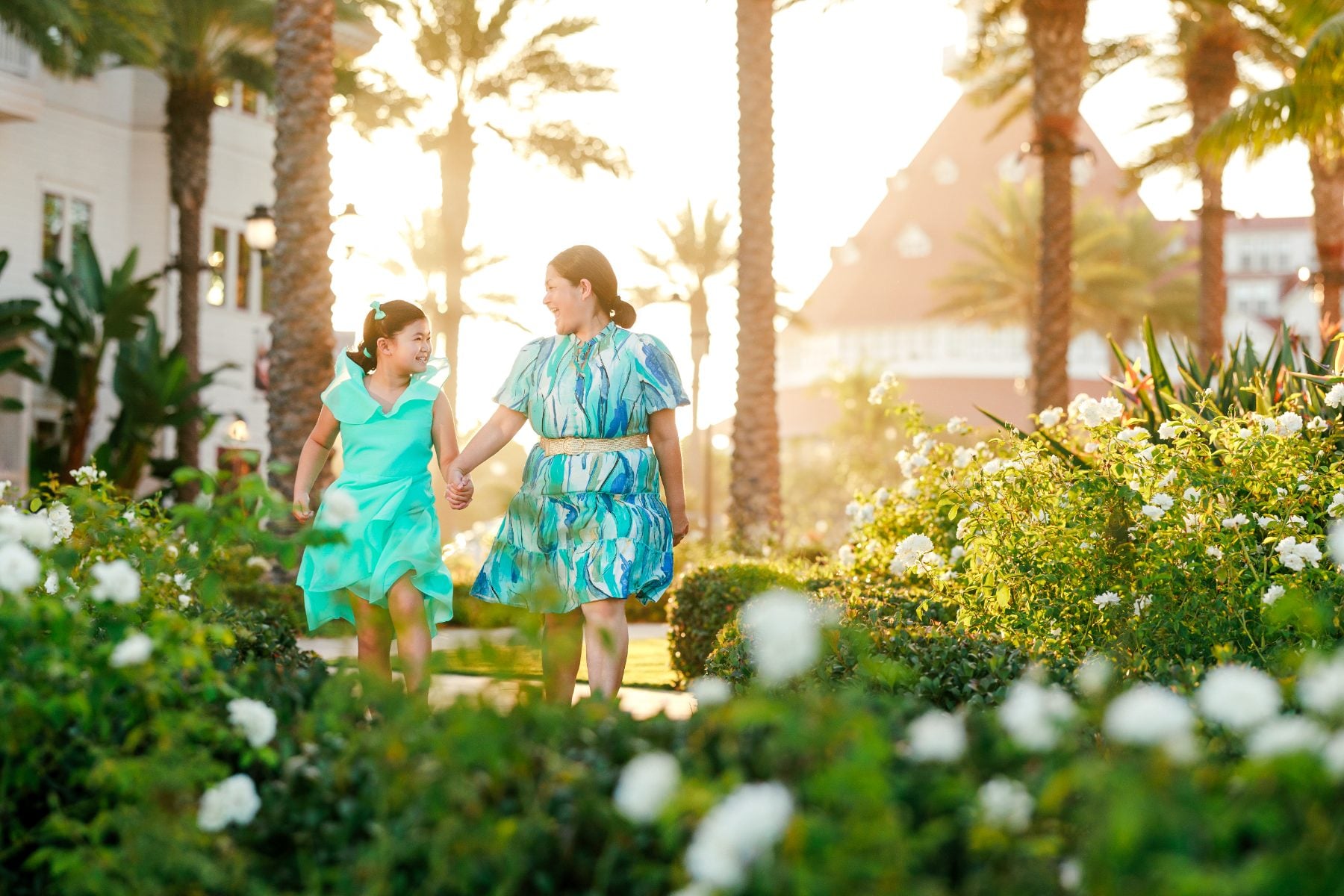 Mother and daughter walking hand in hand through white flower garden at Hotel del Coronado