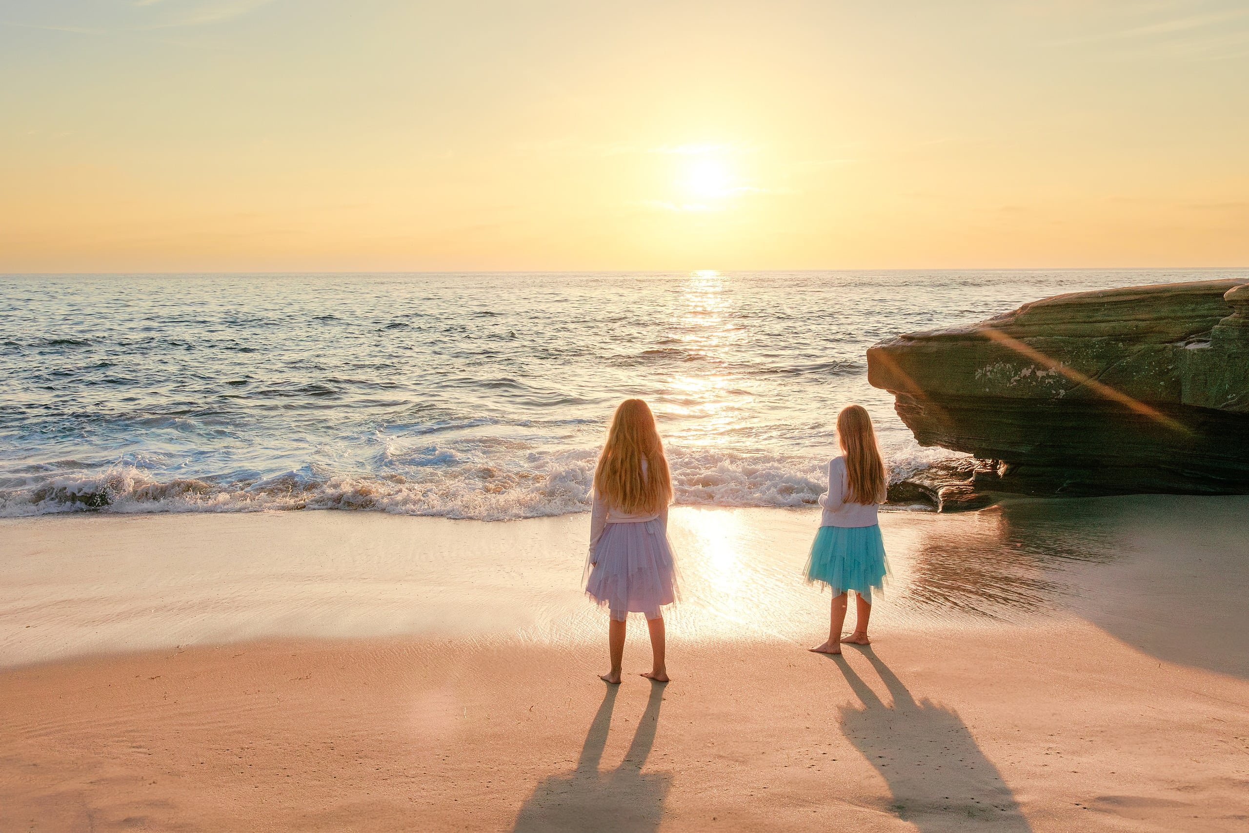 La Jolla Family Photography — 01 Two children in dresses standing on beach at sunset with ocean waves and rocks behind them